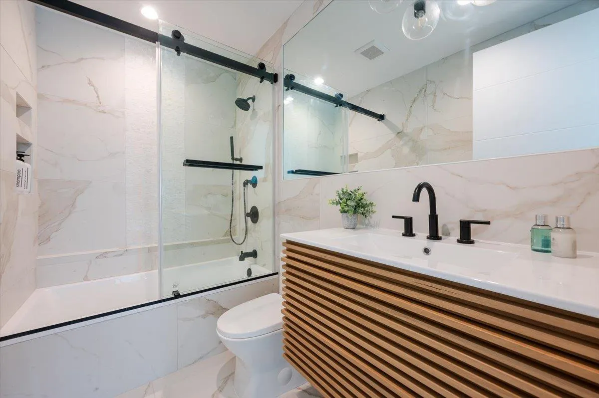 Full bathroom with enclosed tub / shower combo, toilet, vanity, tile walls, and marble finish floors Full bathroom with enclosed tub / shower combo, toilet, vanity, tile walls, and marble finish floors