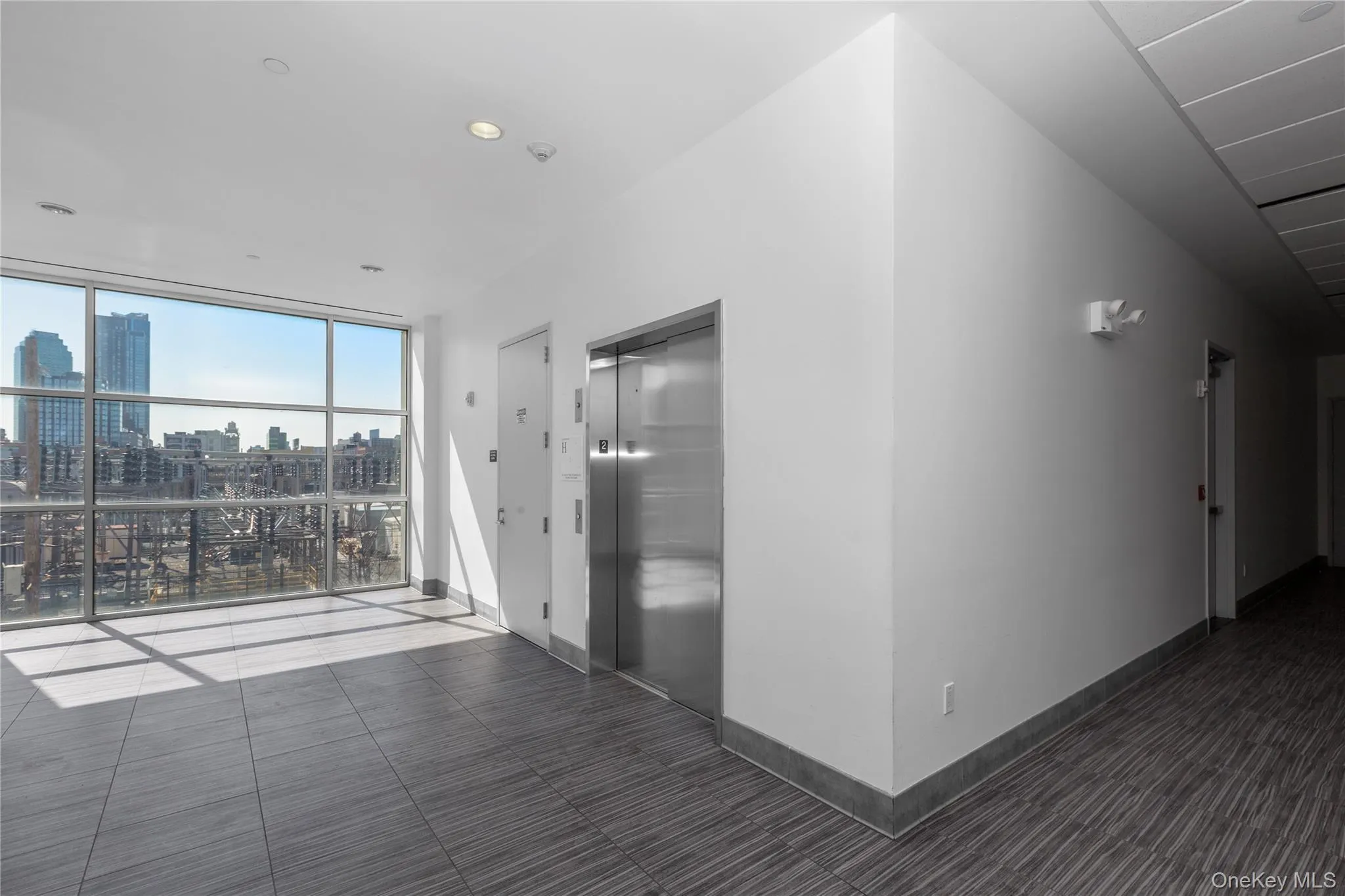 Hallway with elevator, a wall of windows, a city view, baseboards, and recessed lighting Hallway with elevator, a wall of windows, a city view, baseboards, and recessed lighting