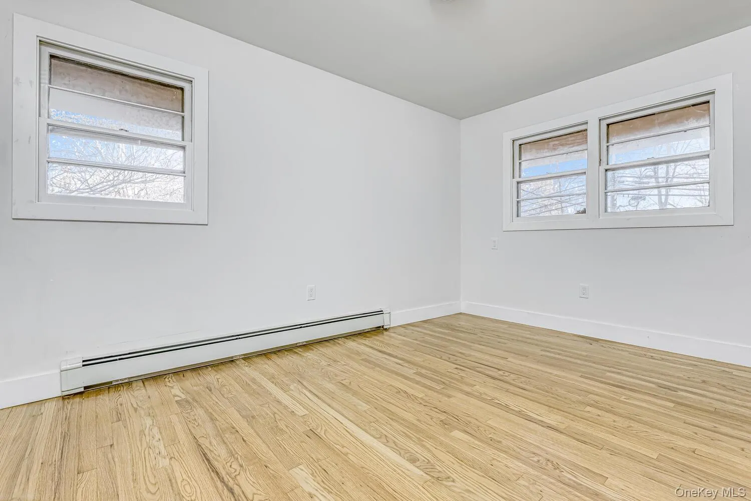 Unfurnished room featuring baseboard heating, light wood-type flooring, and baseboards Unfurnished room featuring baseboard heating, light wood-type flooring, and baseboards