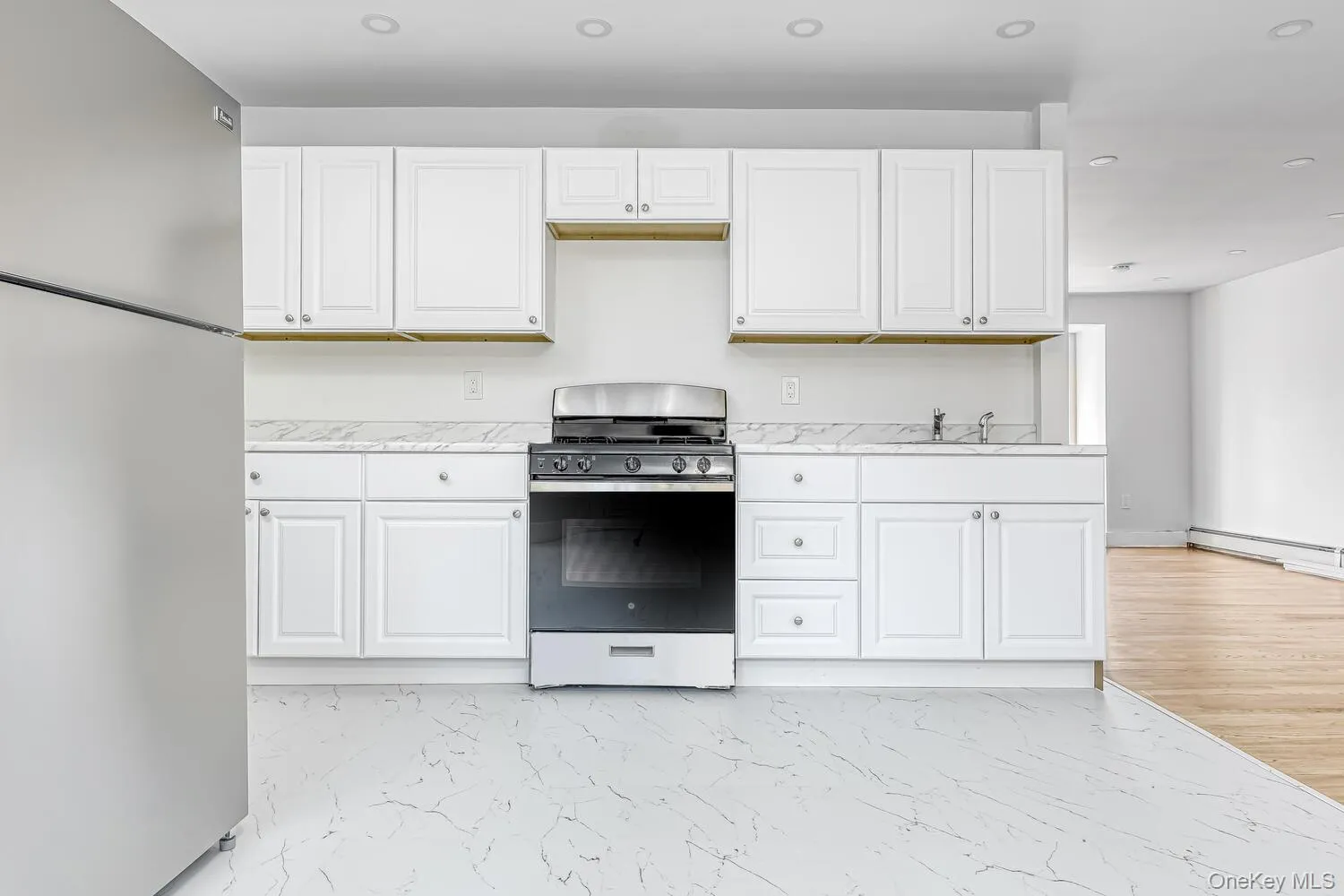 Kitchen featuring stainless steel appliances, white cabinetry, light marble finish floors, a sink, and light stone countertops Kitchen featuring stainless steel appliances, white cabinetry, light marble finish floors, a sink, and light stone countertops