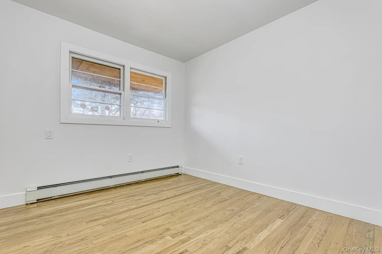 Unfurnished room featuring a baseboard heating unit, light wood-style flooring, and baseboards Unfurnished room featuring a baseboard heating unit, light wood-style flooring, and baseboards