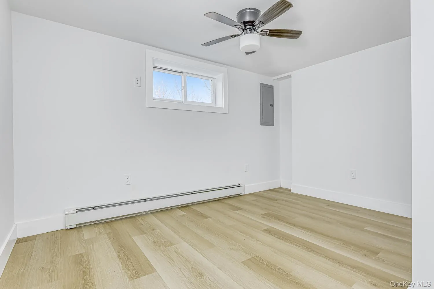 Empty room with a baseboard heating unit, electric panel, wood finished floors, and baseboards Empty room with a baseboard heating unit, electric panel, wood finished floors, and baseboards