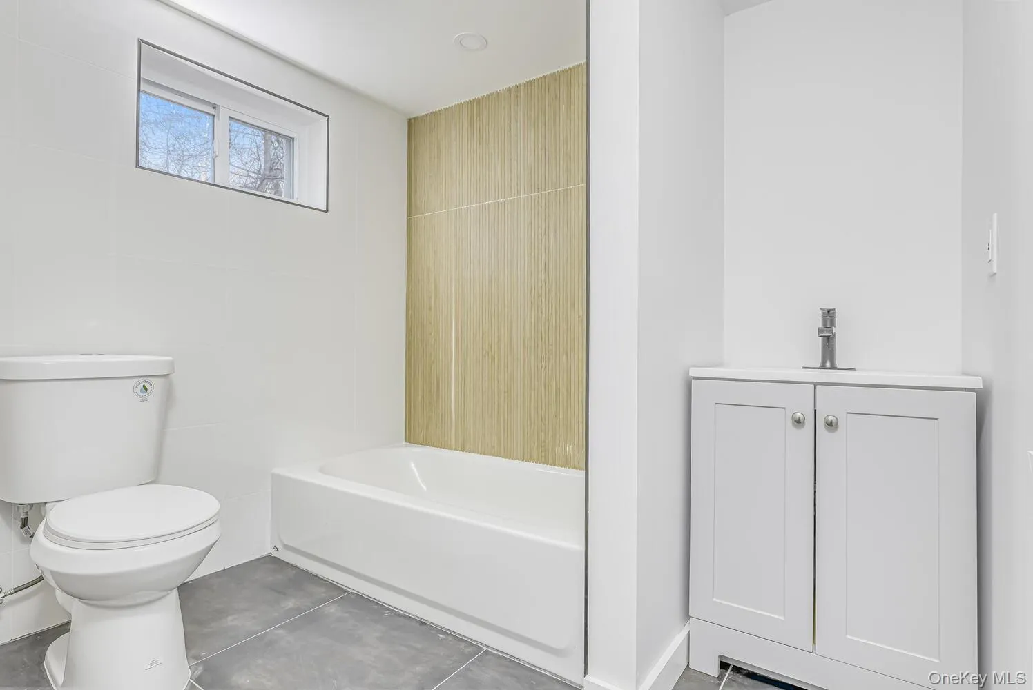 Full bath with toilet, tile walls, a tub to relax in, a sink, and concrete flooring Full bath with toilet, tile walls, a tub to relax in, a sink, and concrete flooring