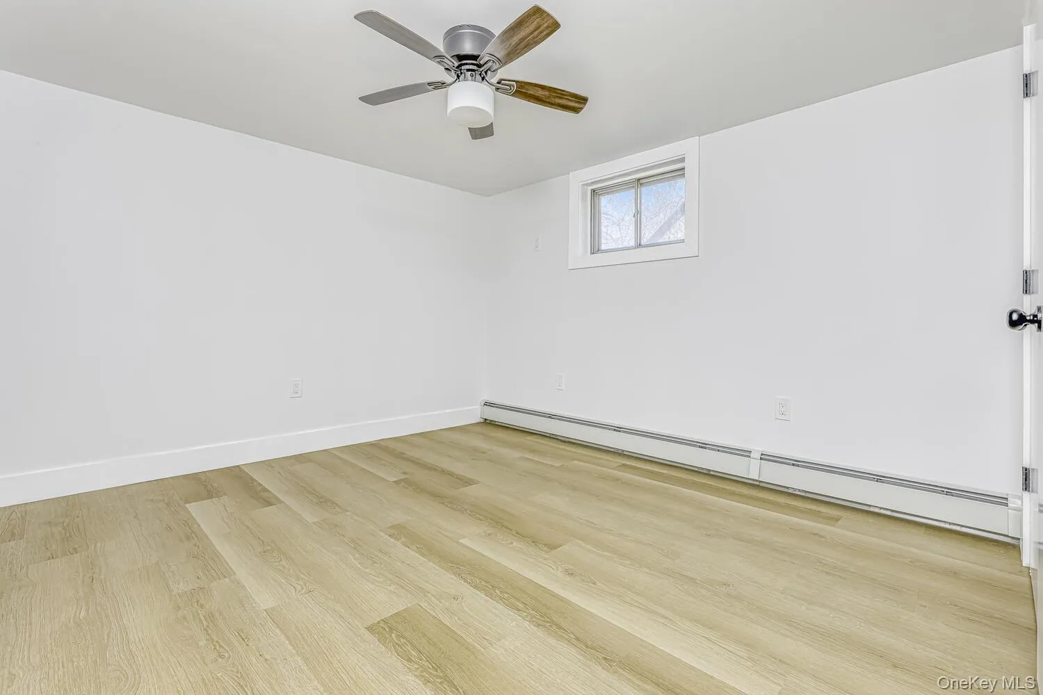 Spare room with baseboard heating, light wood-type flooring, ceiling fan, and baseboards Spare room with baseboard heating, light wood-type flooring, ceiling fan, and baseboards