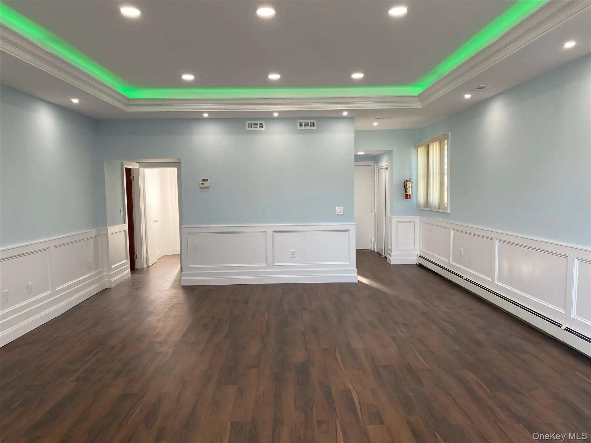 Empty room with a raised ceiling, a baseboard radiator, recessed lighting, dark wood-style floors, and a wainscoted wall Empty room with a raised ceiling, a baseboard radiator, recessed lighting, dark wood-style floors, and a wainscoted wall