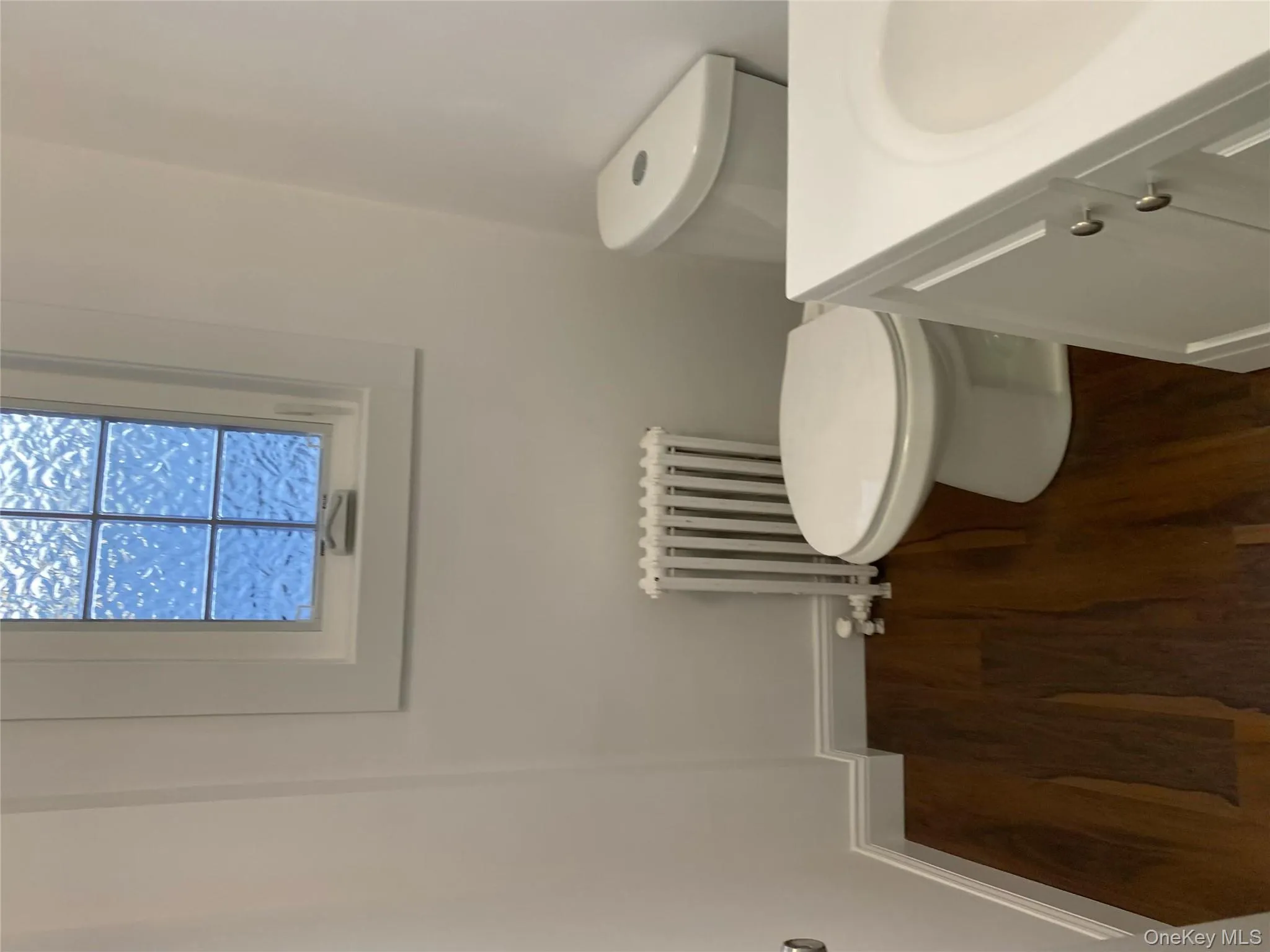 Half bathroom featuring radiator heating unit, wood finished floors, toilet, vanity, and baseboards Half bathroom featuring radiator heating unit, wood finished floors, toilet, vanity, and baseboards