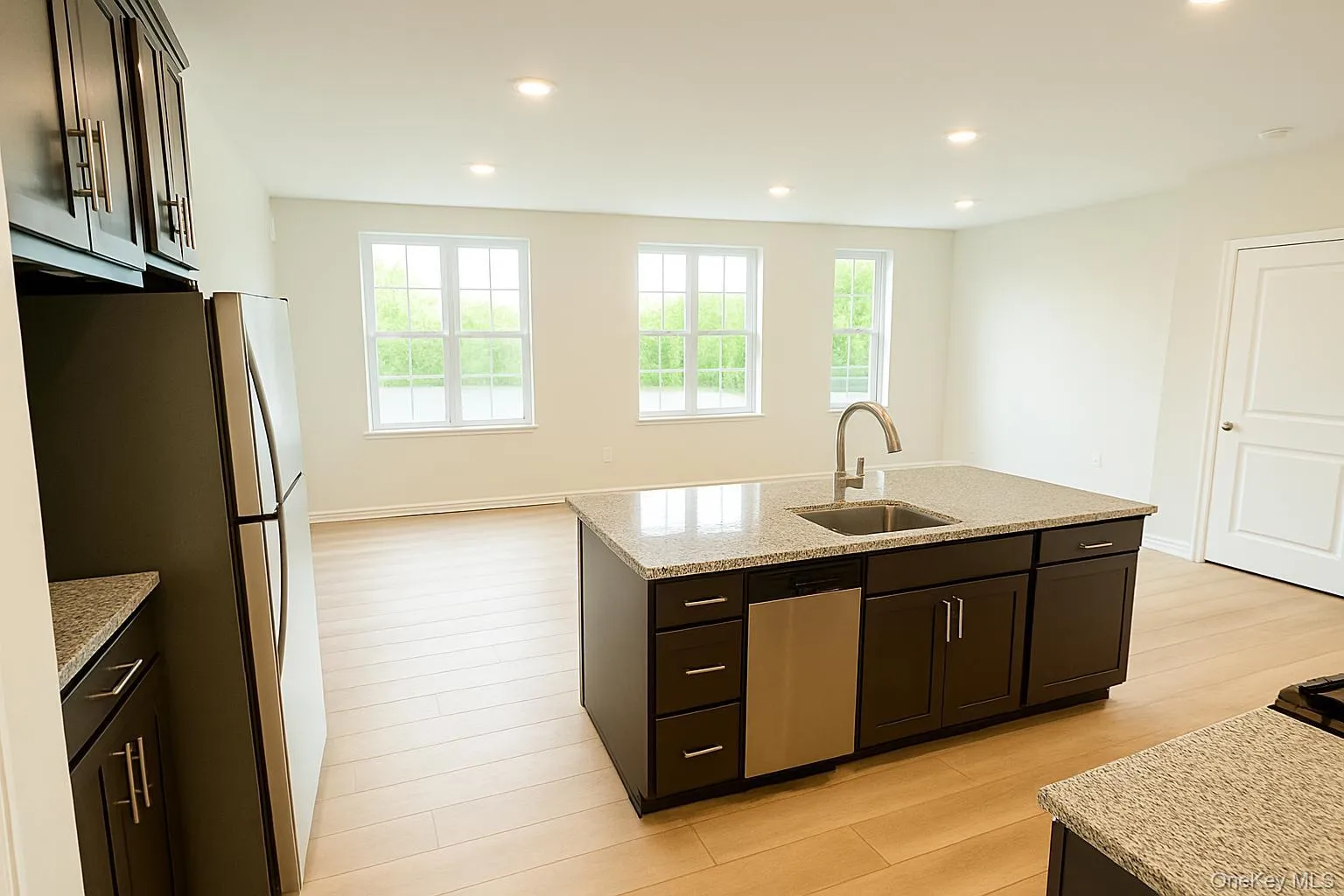 Kitchen featuring stainless steel appliances, a sink, light wood-style flooring, a kitchen island with sink, and light stone counters Kitchen featuring stainless steel appliances, a sink, light wood-style flooring, a kitchen island with sink, and light stone counters