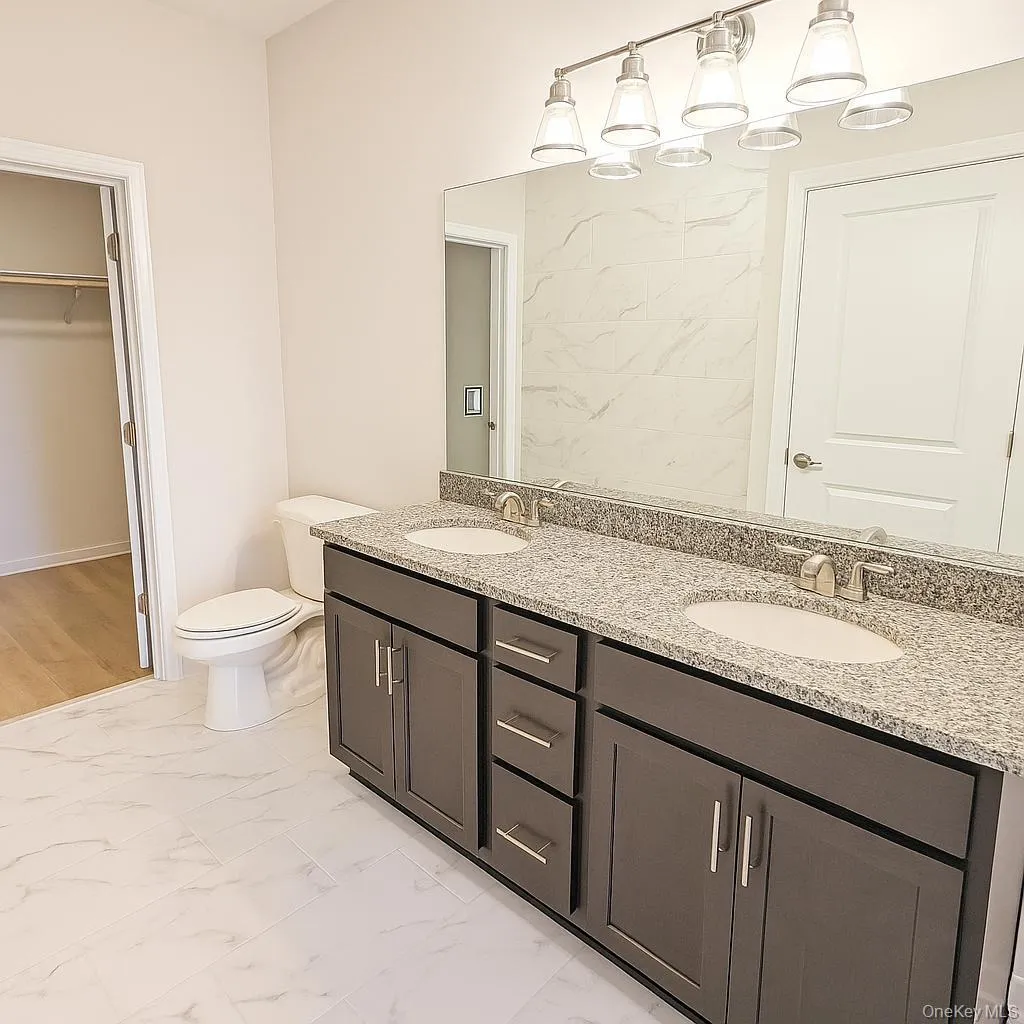 Full bath with marble look tiles, toilet, double vanity, and a walk in closet Full bath with marble look tiles, toilet, double vanity, and a walk in closet