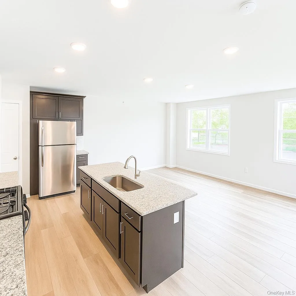 Kitchen with freestanding refrigerator, a sink, light wood-style flooring, dark brown cabinetry, and light stone counters Kitchen with freestanding refrigerator, a sink, light wood-style flooring, dark brown cabinetry, and light stone counters