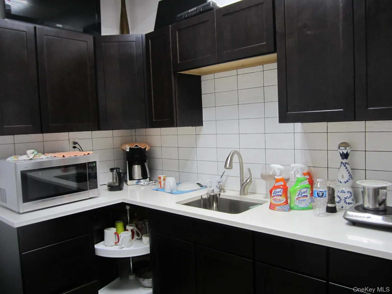 Kitchen with stainless steel microwave, dark cabinets, a sink, and backsplash Kitchen with stainless steel microwave, dark cabinets, a sink, and backsplash
