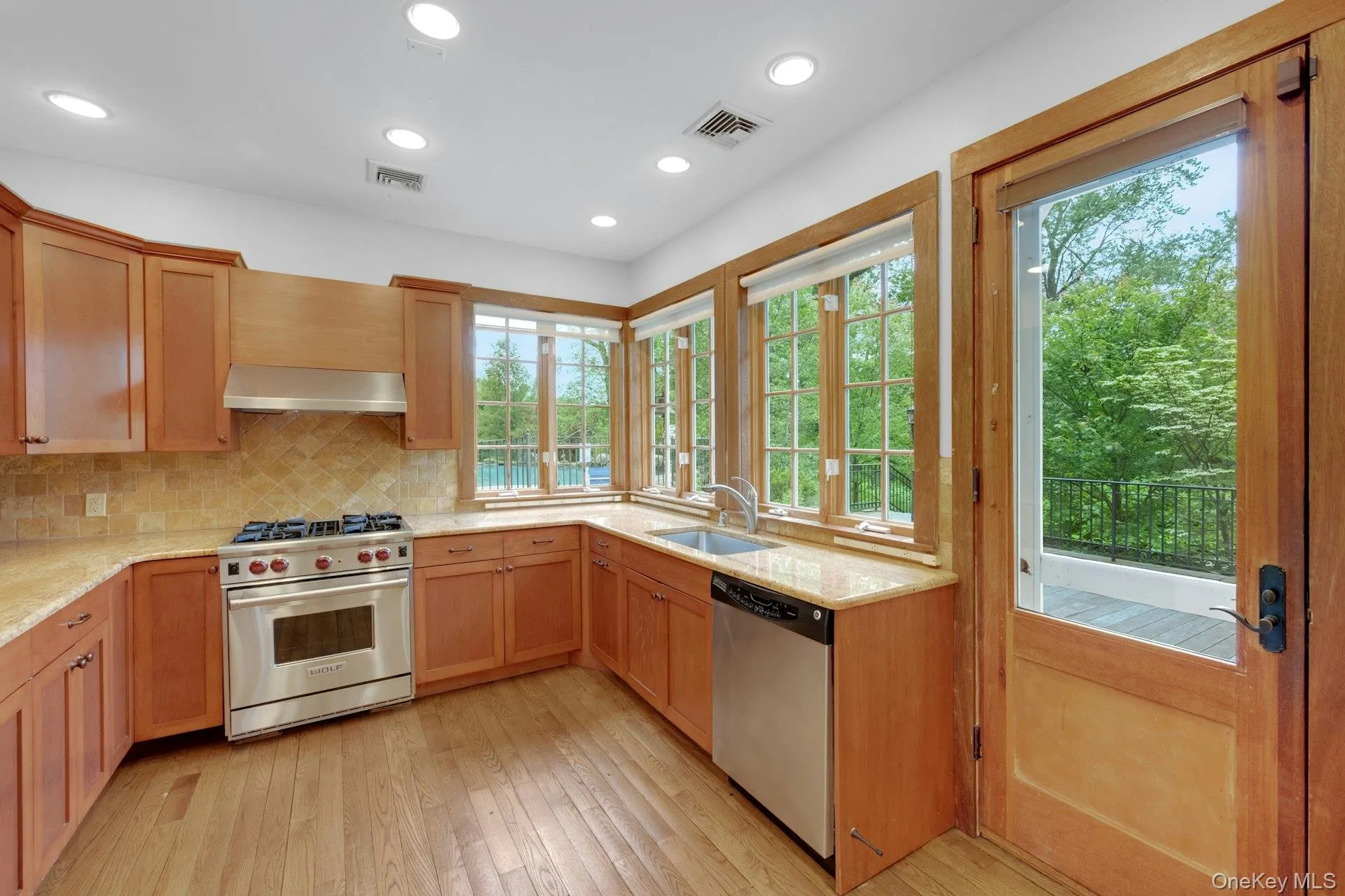 Pool House w/full Kitchen featuring stainless steel appliances, wall chimney range hood, a sink, decorative backsplash, and light stone counters Pool House w/full Kitchen featuring stainless steel appliances, wall chimney range hood, a sink, decorative backsplash, and light stone counters