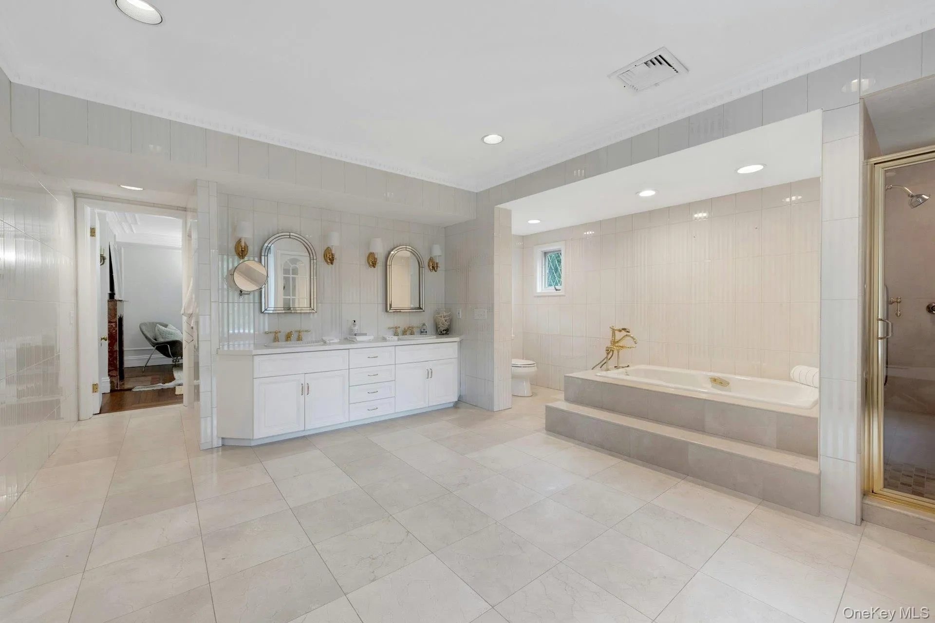 Spacious primary bedroom ensuite full bathroom featuring crown molding, tile walls, tile patterned flooring, a garden tub, and double vanity Spacious primary bedroom ensuite full bathroom featuring crown molding, tile walls, tile patterned flooring, a garden tub, and double vanity