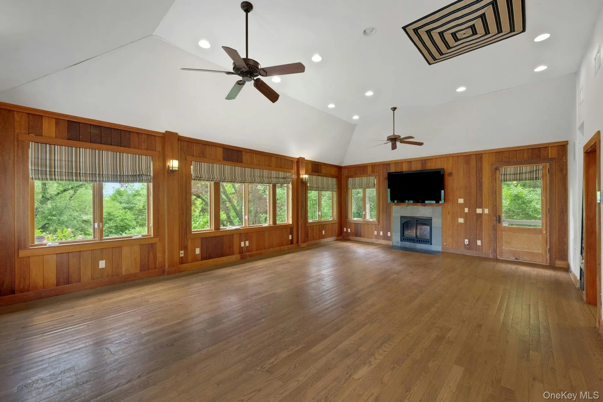 Pool house featuring ceiling fan, high vaulted ceiling, plenty of natural light, wooden walls, and a tiled fireplace Pool house featuring ceiling fan, high vaulted ceiling, plenty of natural light, wooden walls, and a tiled fireplace