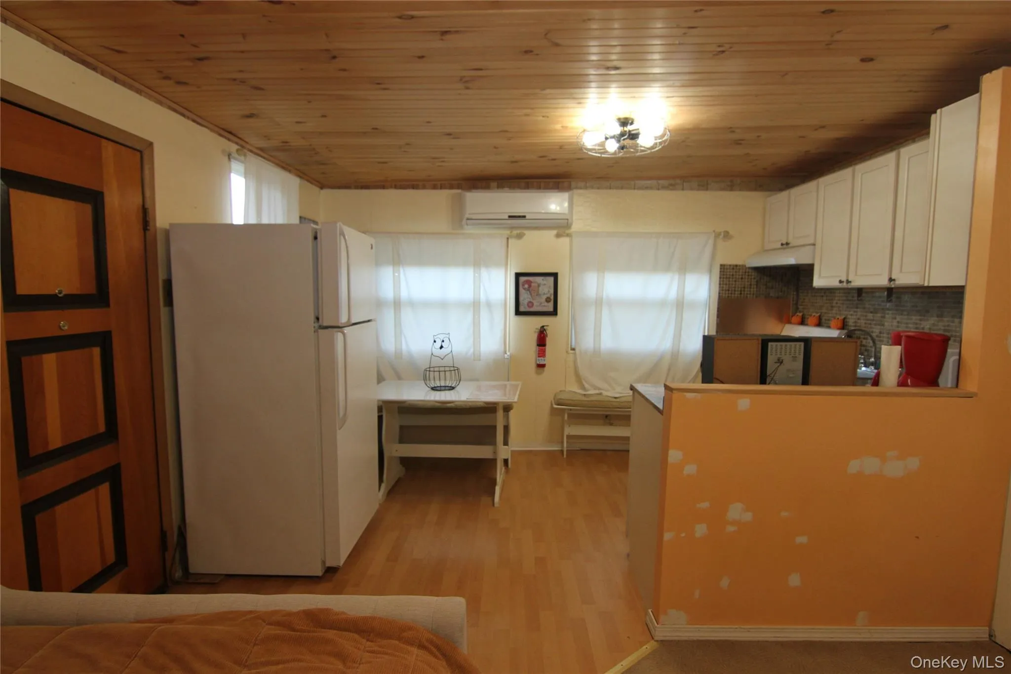Kitchen featuring freestanding refrigerator, under cabinet range hood, a wall mounted AC, wood ceiling, and light wood finished floors Kitchen featuring freestanding refrigerator, under cabinet range hood, a wall mounted AC, wood ceiling, and light wood finished floors