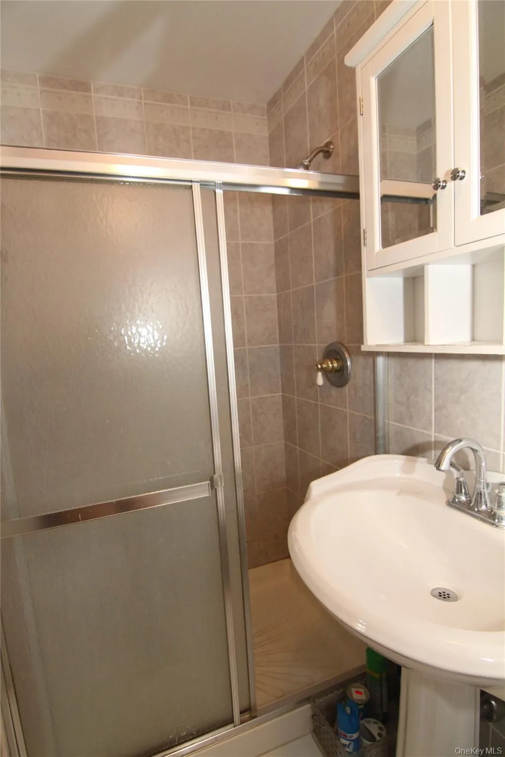 Bathroom with a shower stall, tile walls, and a sink Bathroom with a shower stall, tile walls, and a sink