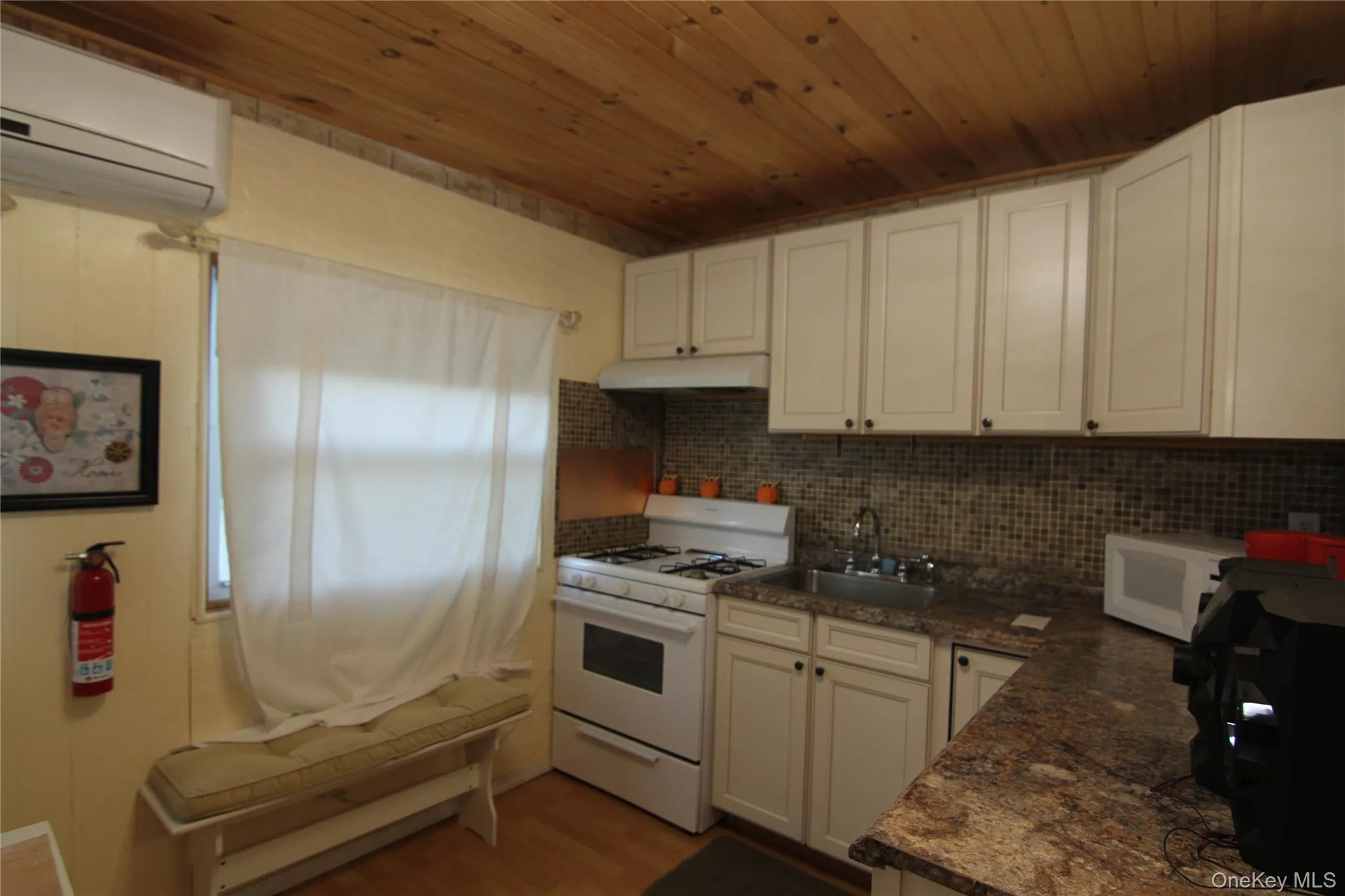 Kitchen with white appliances, under cabinet range hood, a wall mounted AC, a sink, and dark countertops Kitchen with white appliances, under cabinet range hood, a wall mounted AC, a sink, and dark countertops
