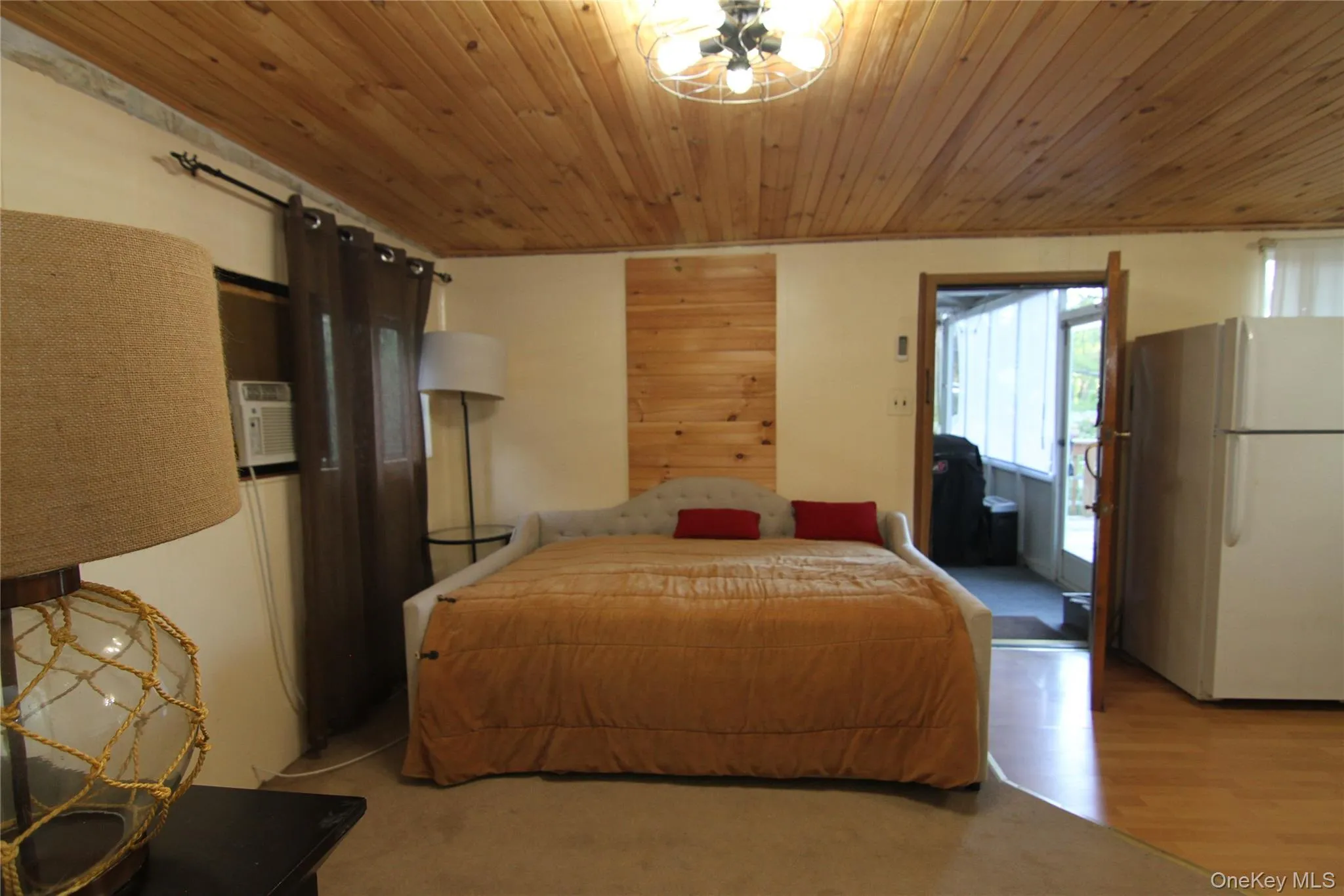 Bedroom featuring freestanding refrigerator, wooden ceiling, and wood finished floors Bedroom featuring freestanding refrigerator, wooden ceiling, and wood finished floors