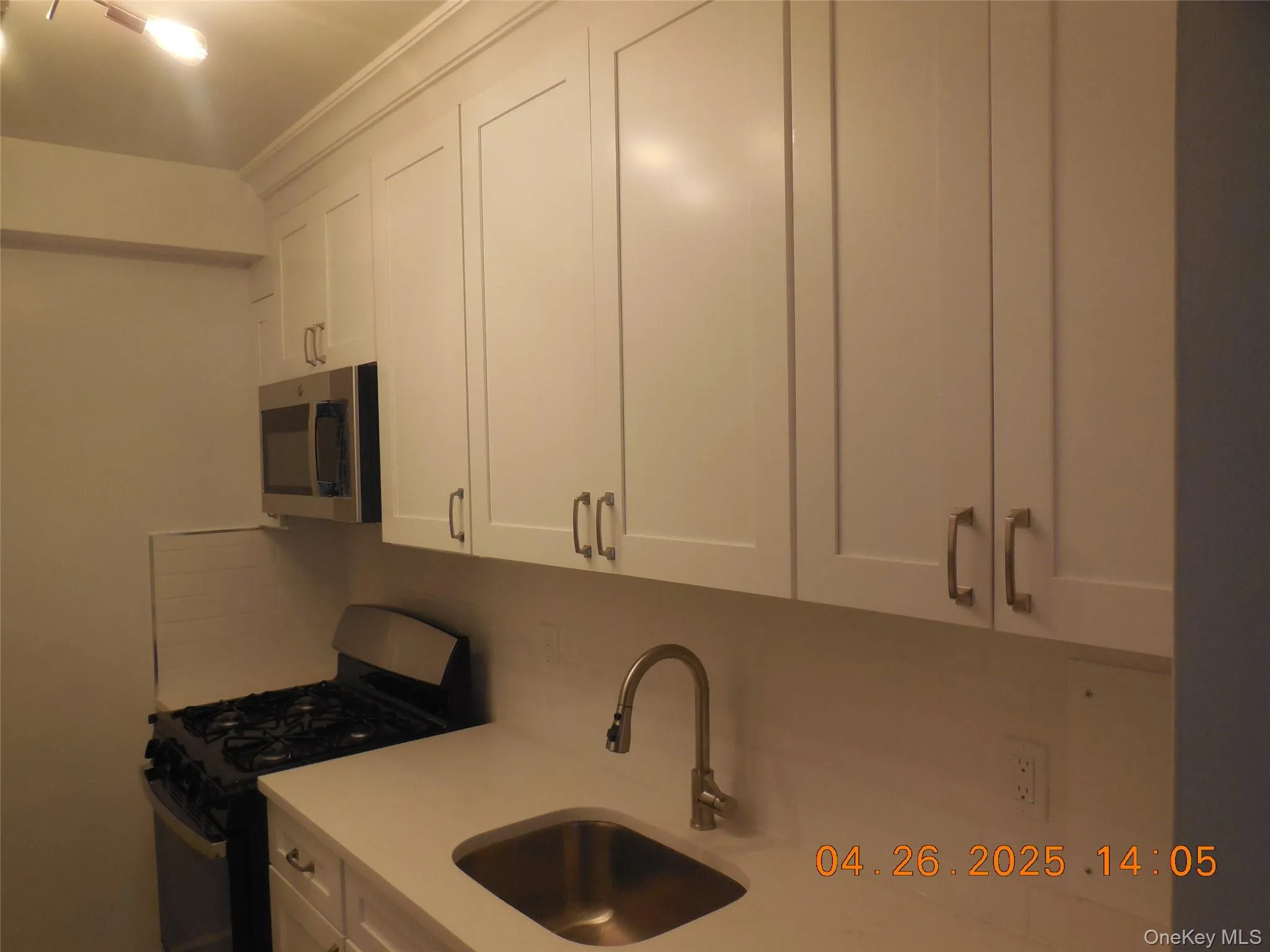 Kitchen with stainless steel appliances, a sink, backsplash, light countertops, and white cabinetry Kitchen with stainless steel appliances, a sink, backsplash, light countertops, and white cabinetry