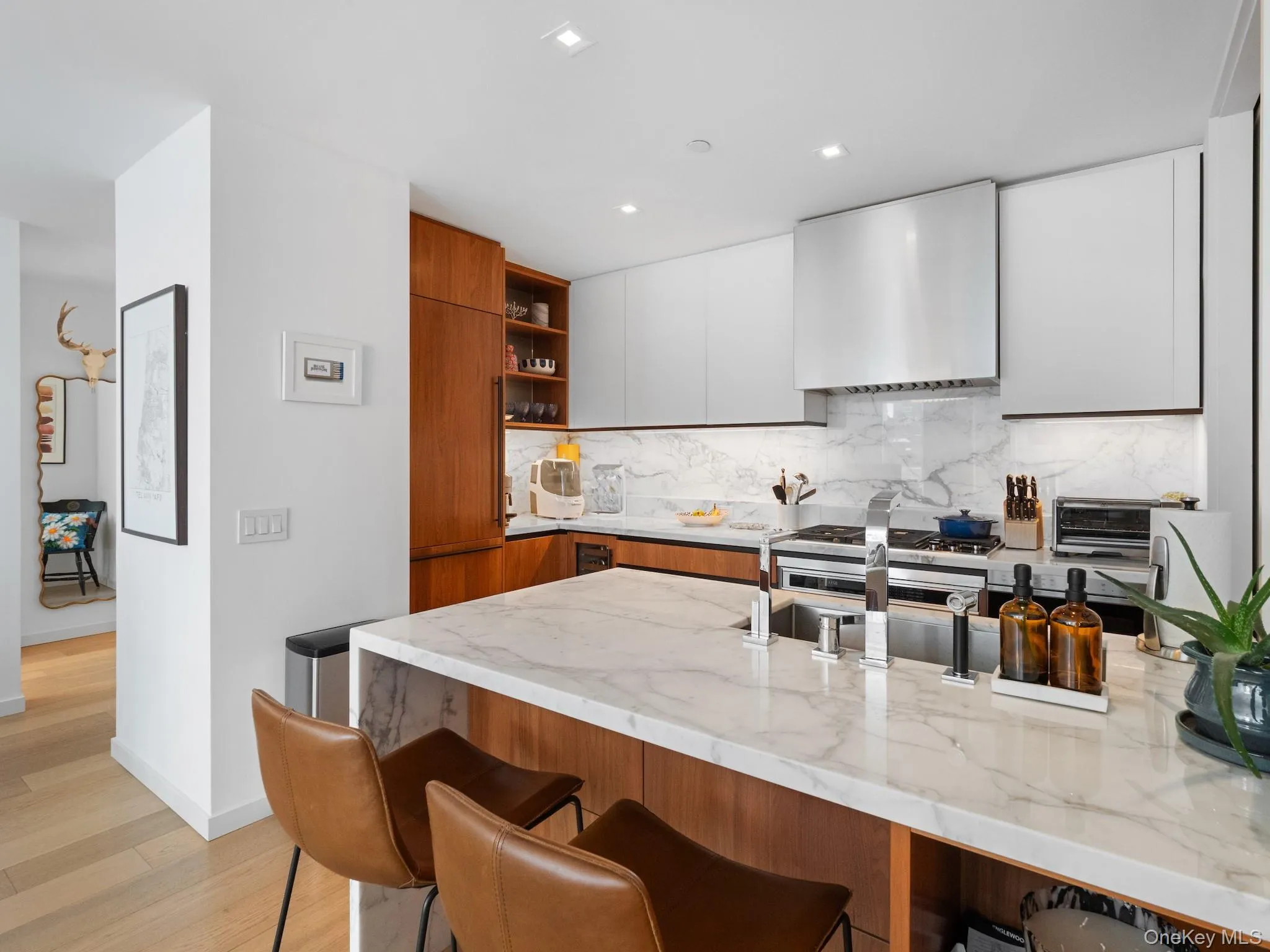 Kitchen featuring wall chimney exhaust hood, open shelves, modern cabinets, a breakfast bar, and light stone counters Kitchen featuring wall chimney exhaust hood, open shelves, modern cabinets, a breakfast bar, and light stone counters