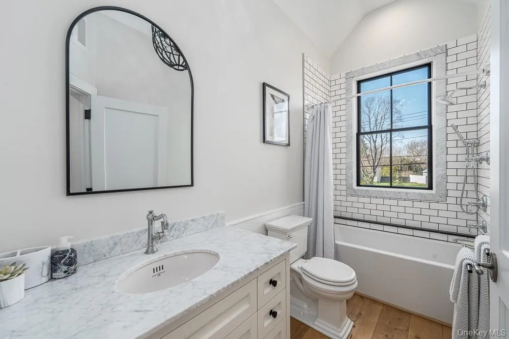 Bathroom featuring wood finished floors, toilet, vanity, lofted ceiling, and shower / bath combo Bathroom featuring wood finished floors, toilet, vanity, lofted ceiling, and shower / bath combo