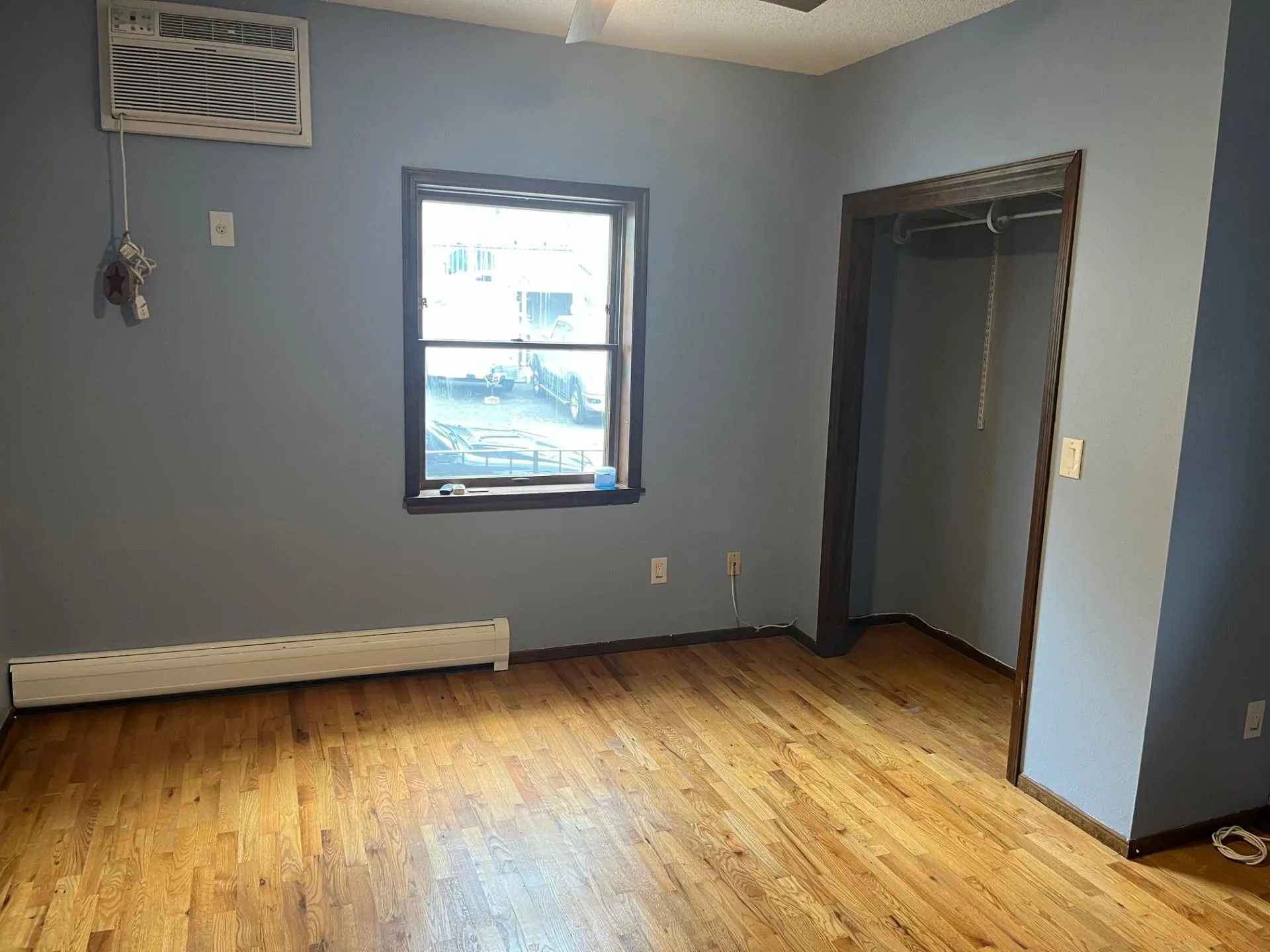 Unfurnished bedroom featuring light wood-style flooring, baseboard heating, and a wall unit AC Unfurnished bedroom featuring light wood-style flooring, baseboard heating, and a wall unit AC
