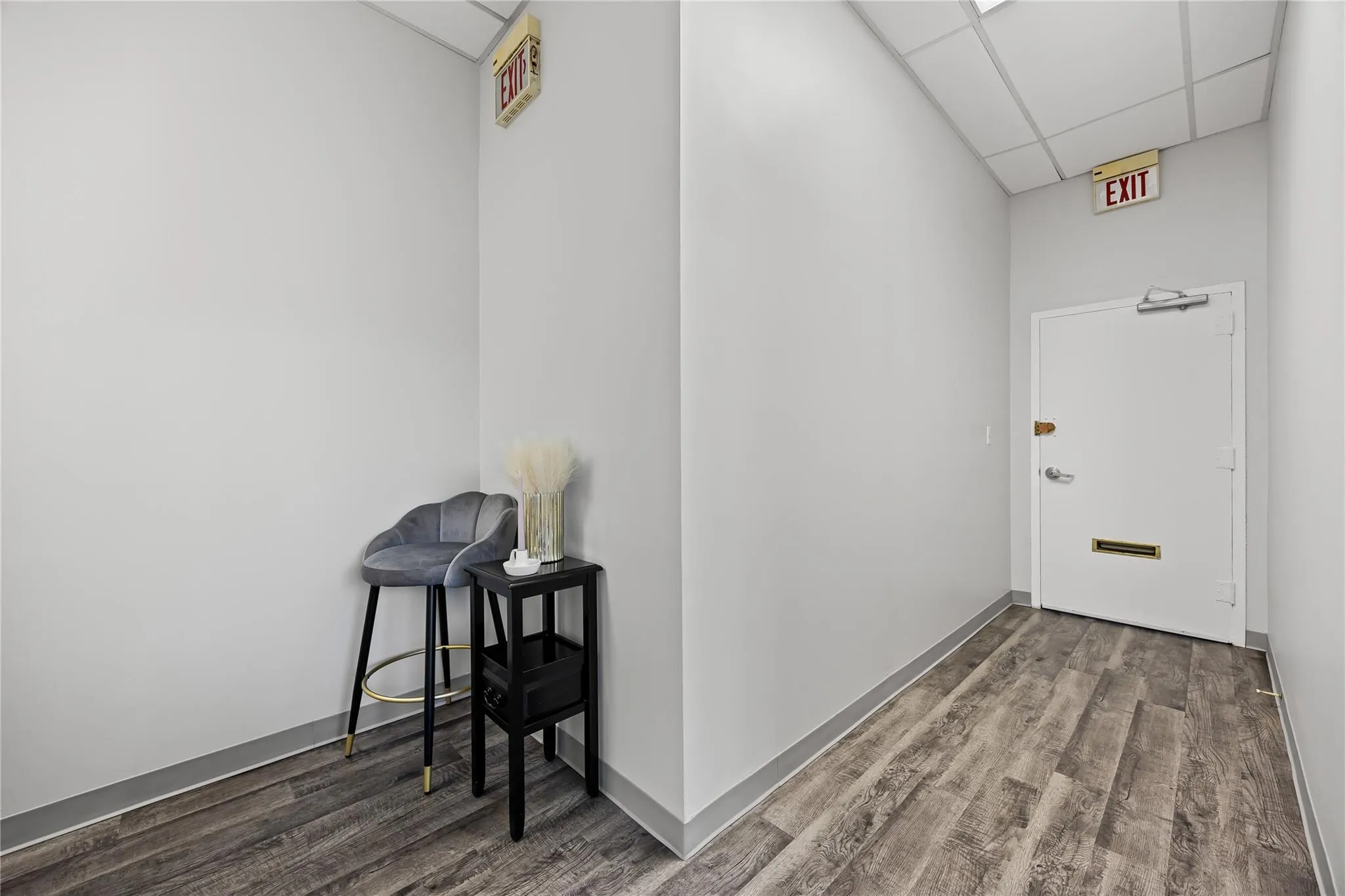 Corridor featuring wood finished floors, a drop ceiling, and baseboards Corridor featuring wood finished floors, a drop ceiling, and baseboards