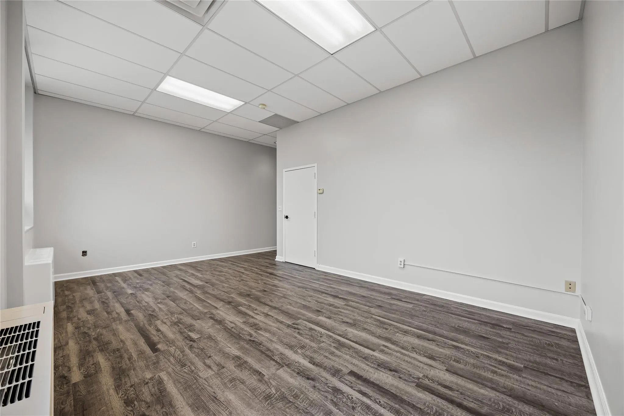 Empty room featuring dark wood-type flooring, a paneled ceiling, and baseboards Empty room featuring dark wood-type flooring, a paneled ceiling, and baseboards