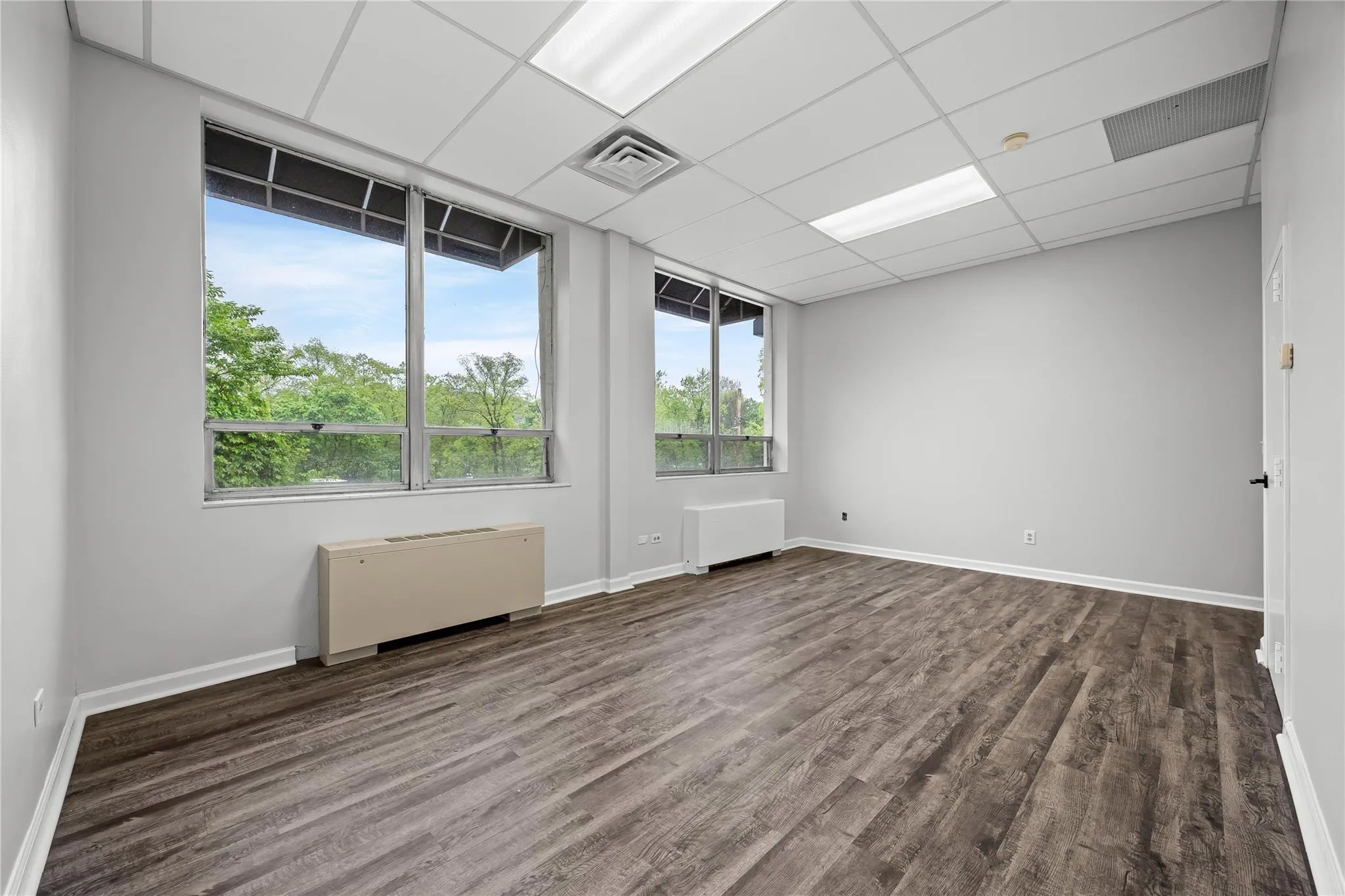 Spare room with radiator, dark wood-style flooring, baseboards, and a drop ceiling Spare room with radiator, dark wood-style flooring, baseboards, and a drop ceiling