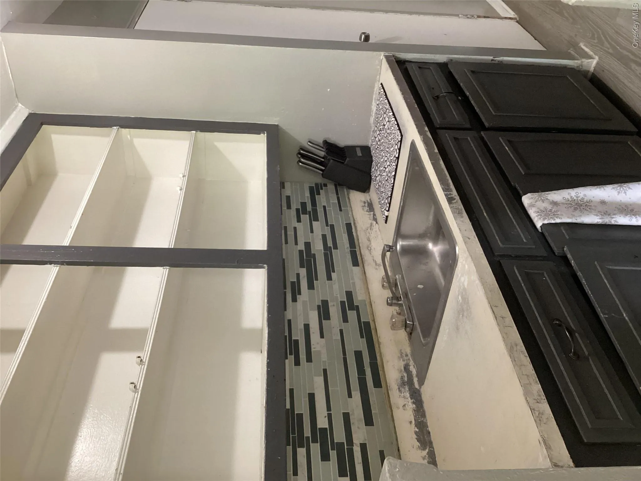 Kitchen with open shelves, a sink, tasteful backsplash, light wood-type flooring, and dark cabinetry Kitchen with open shelves, a sink, tasteful backsplash, light wood-type flooring, and dark cabinetry