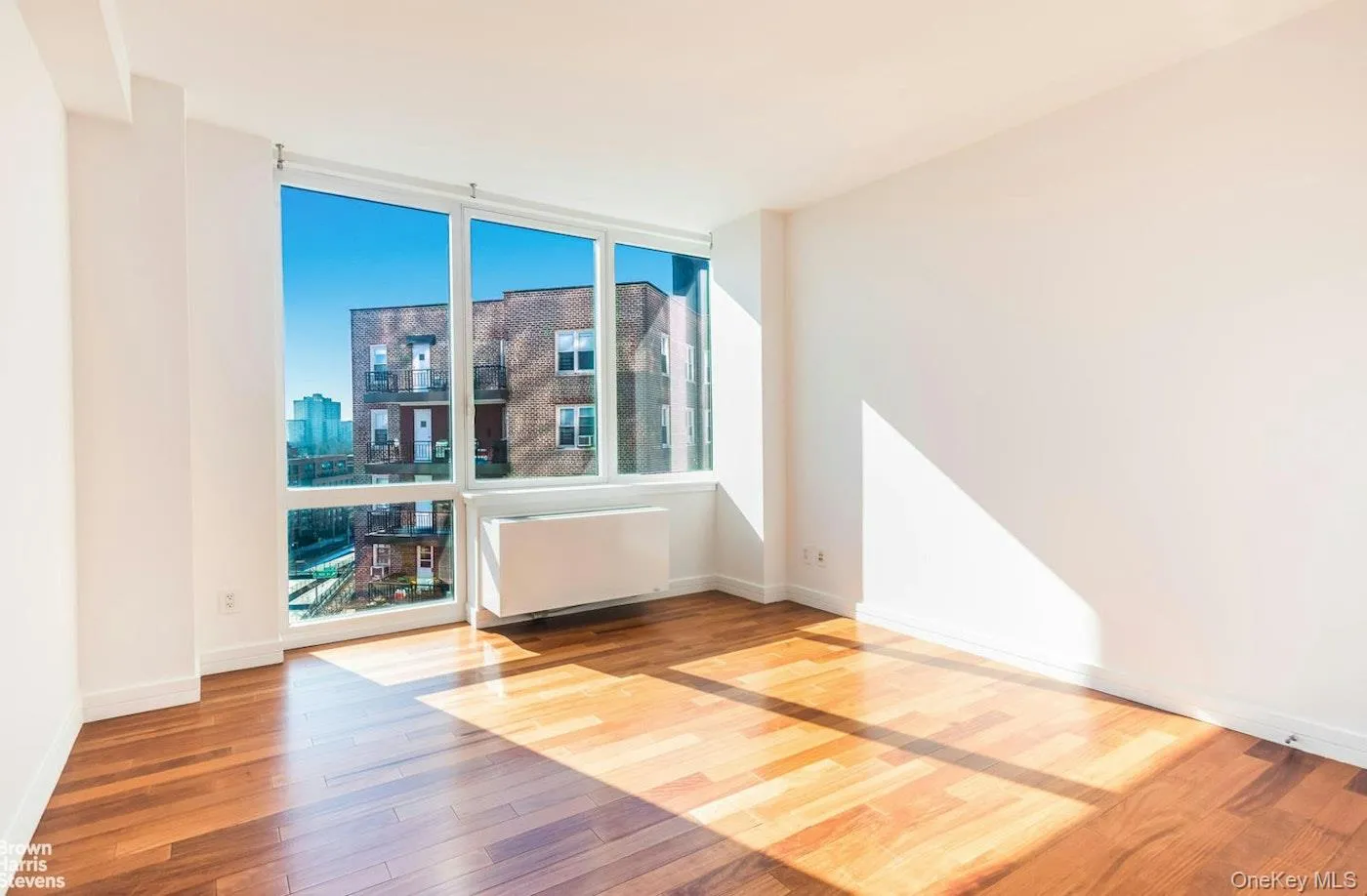Unfurnished room featuring wood-type flooring, radiator heating unit, floor to ceiling windows, a city view, and baseboards Unfurnished room featuring wood-type flooring, radiator heating unit, floor to ceiling windows, a city view, and baseboards