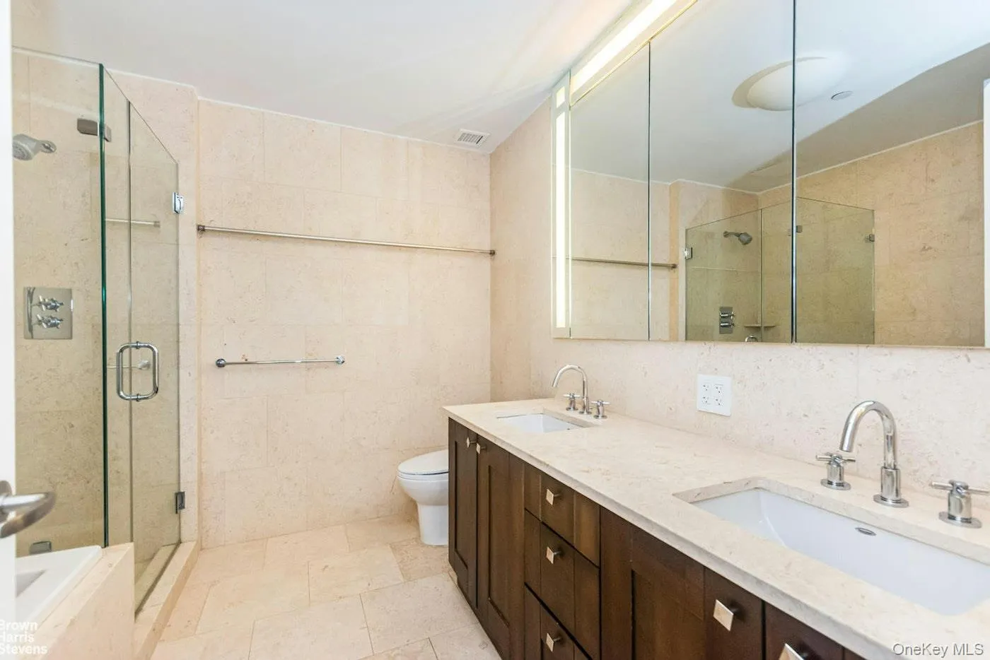 Full bathroom featuring tile walls, a shower stall, toilet, and double vanity Full bathroom featuring tile walls, a shower stall, toilet, and double vanity