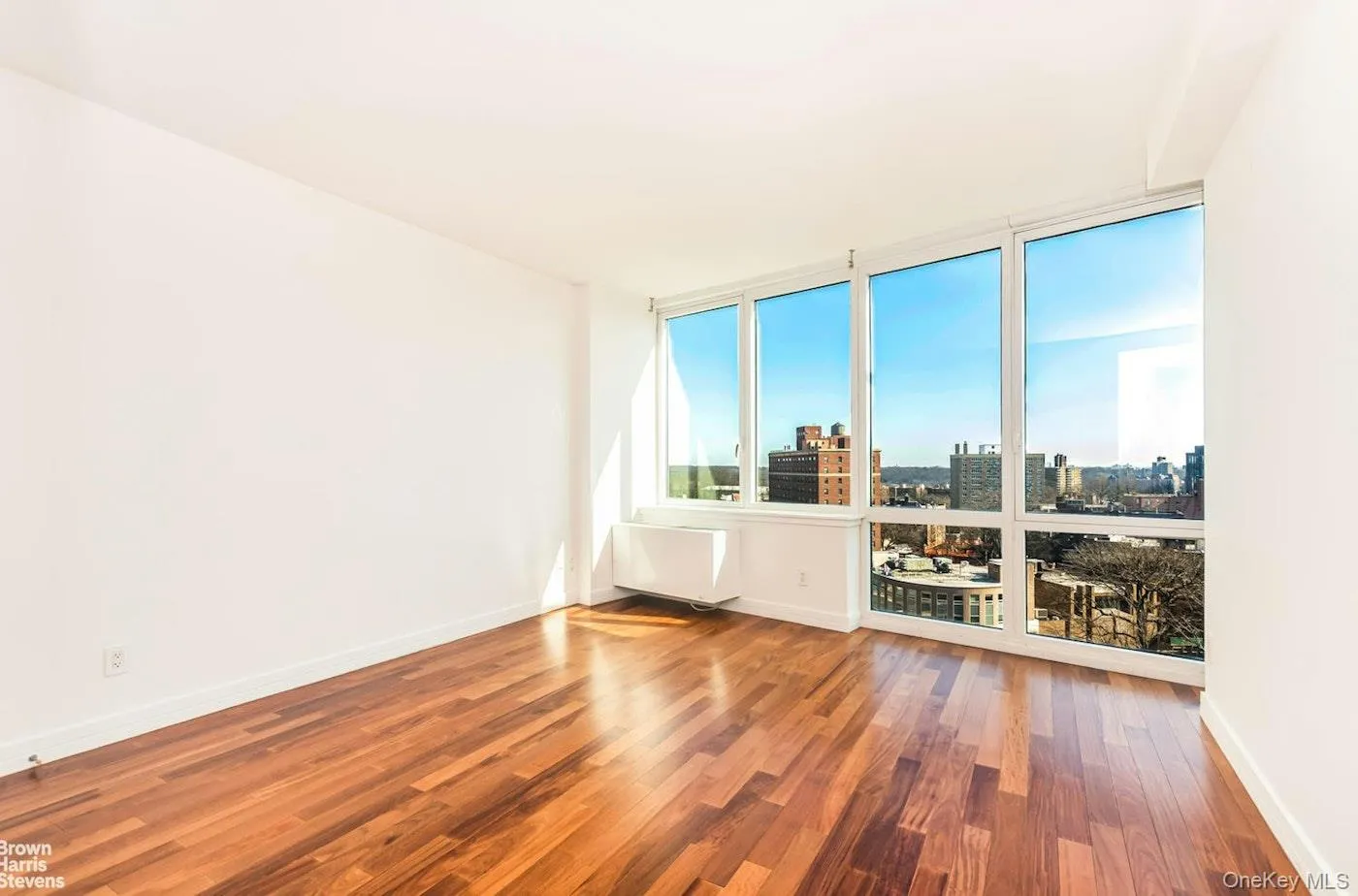 Empty room with wood finished floors, baseboards, a view of city, and floor to ceiling windows Empty room with wood finished floors, baseboards, a view of city, and floor to ceiling windows