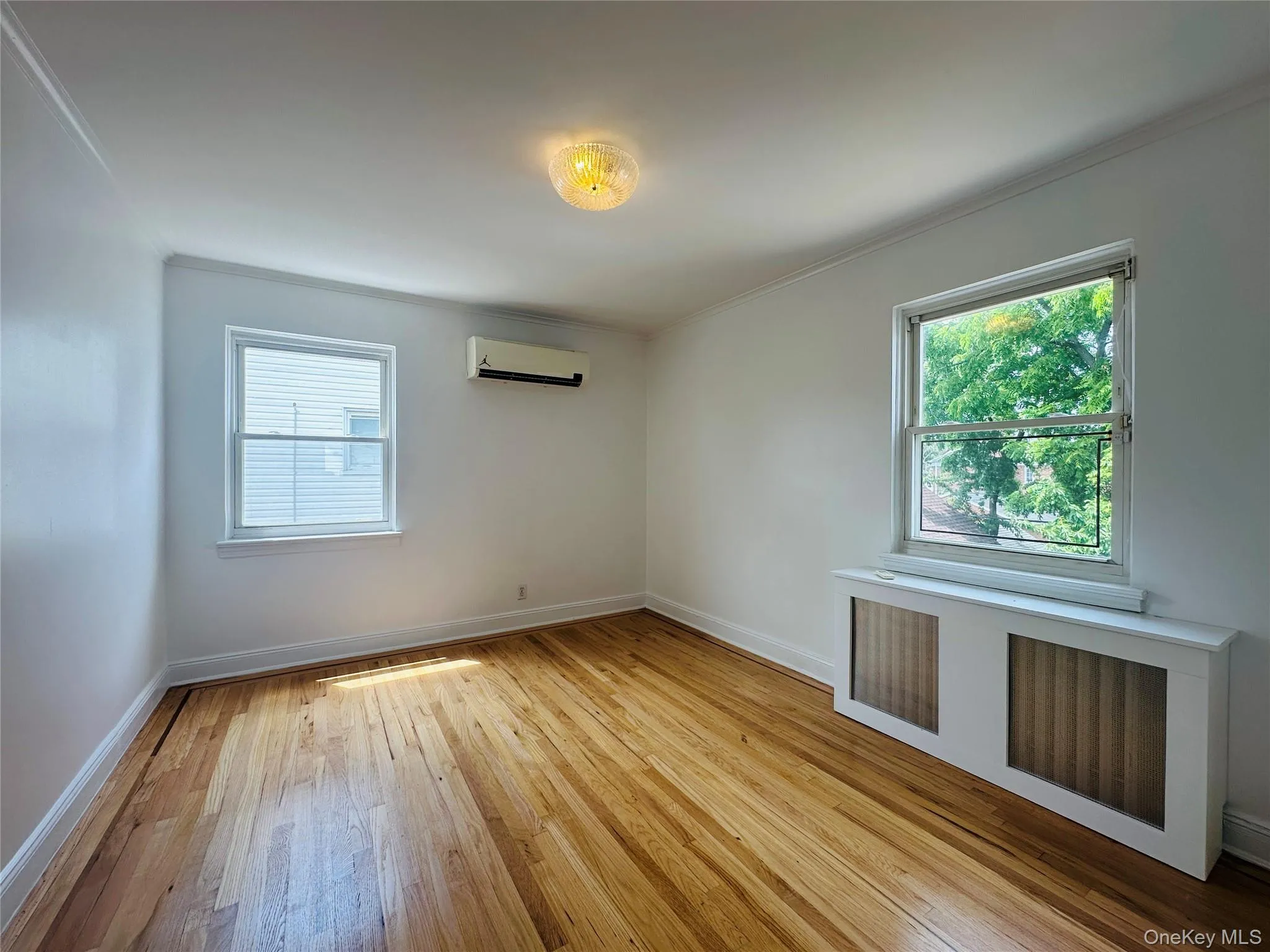 Spare room featuring radiator heating unit, hardwood / wood-style floors, crown molding, healthy amount of natural light, and an AC wall unit Spare room featuring radiator heating unit, hardwood / wood-style floors, crown molding, healthy amount of natural light, and an AC wall unit