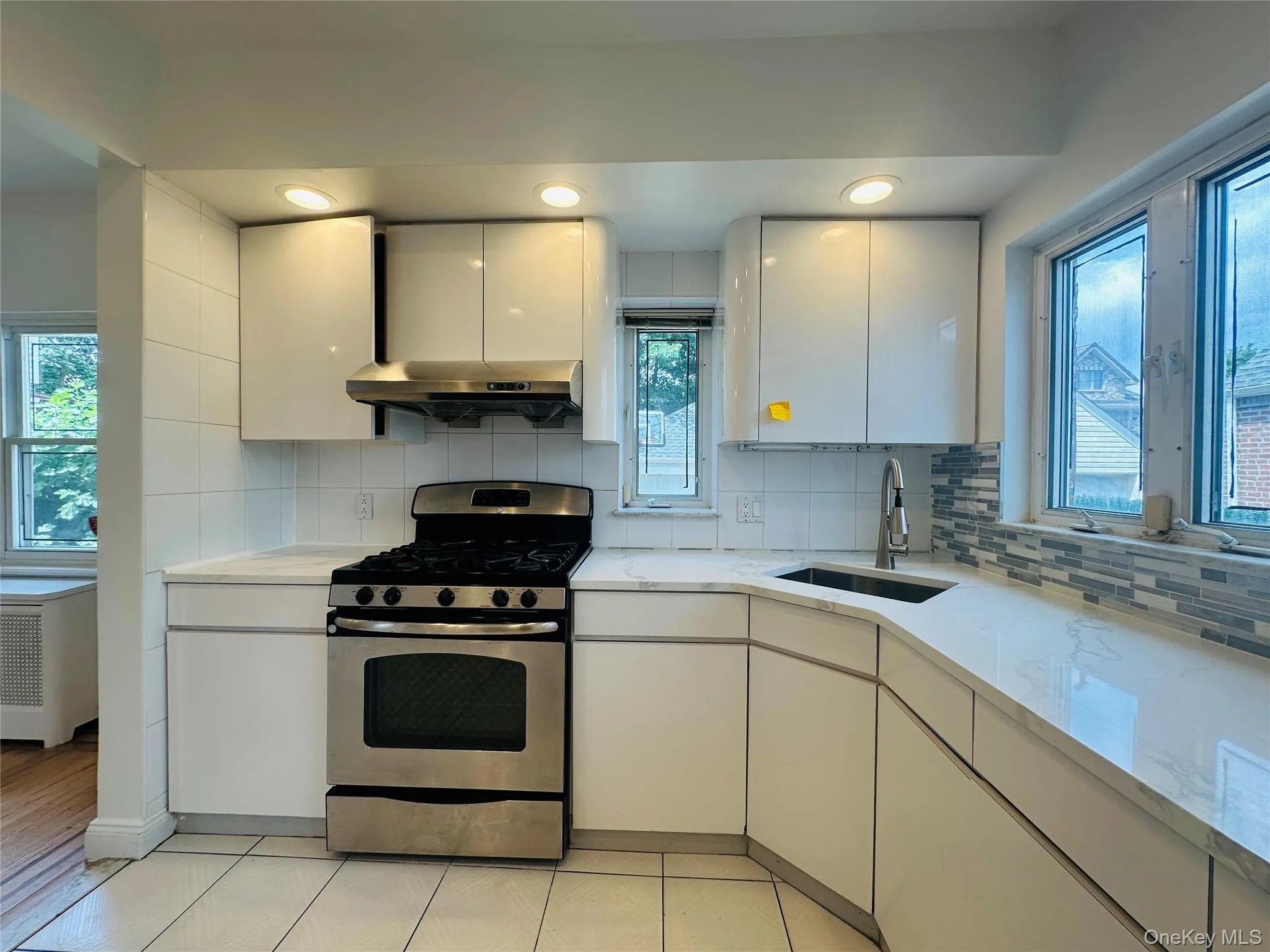 Kitchen featuring stainless steel gas range, tasteful backsplash, white cabinetry, wall chimney exhaust hood, and radiator heating unit Kitchen featuring stainless steel gas range, tasteful backsplash, white cabinetry, wall chimney exhaust hood, and radiator heating unit