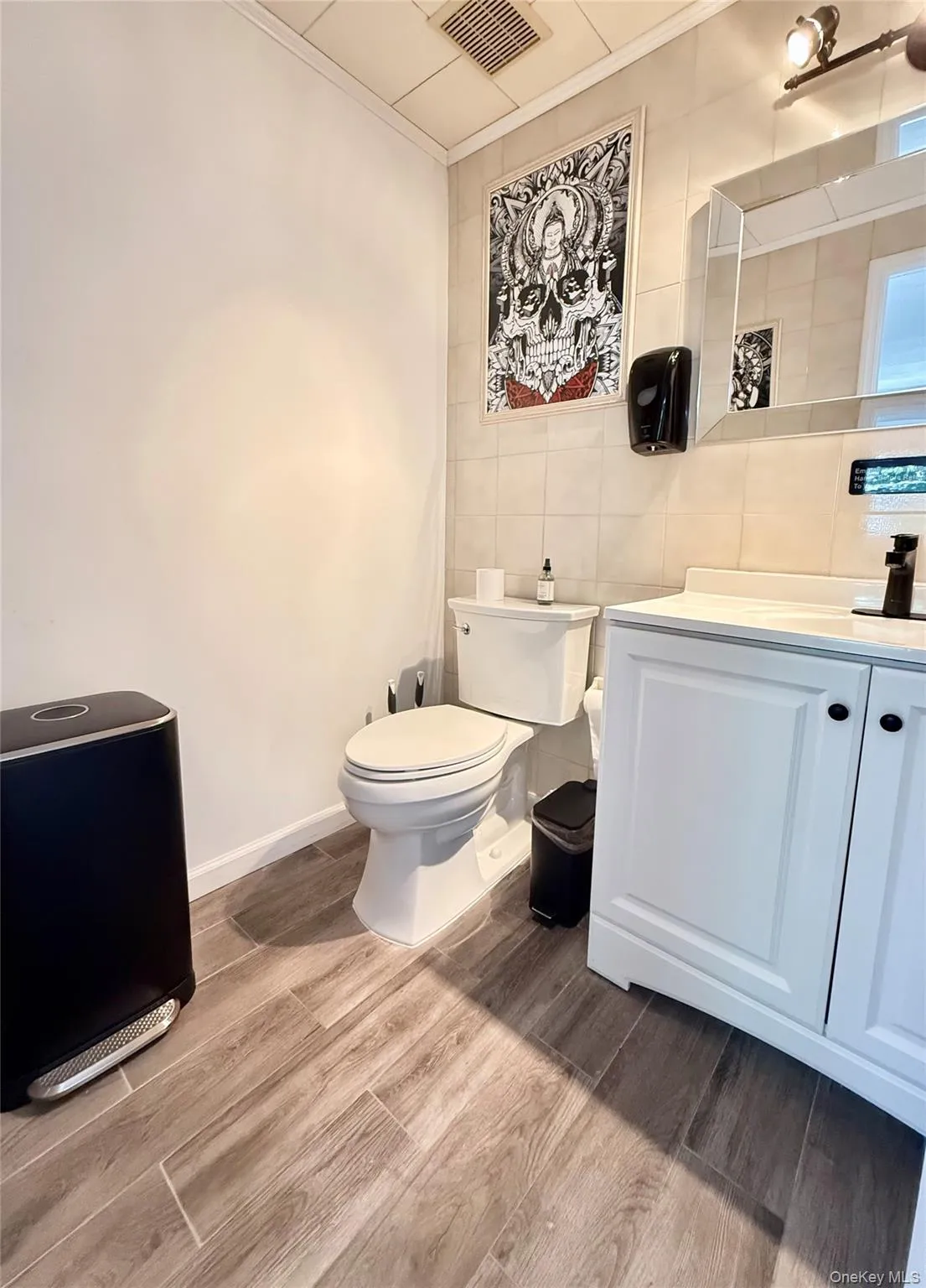 Half bathroom featuring tile walls, toilet, wood finished floors, ornamental molding, and vanity Half bathroom featuring tile walls, toilet, wood finished floors, ornamental molding, and vanity