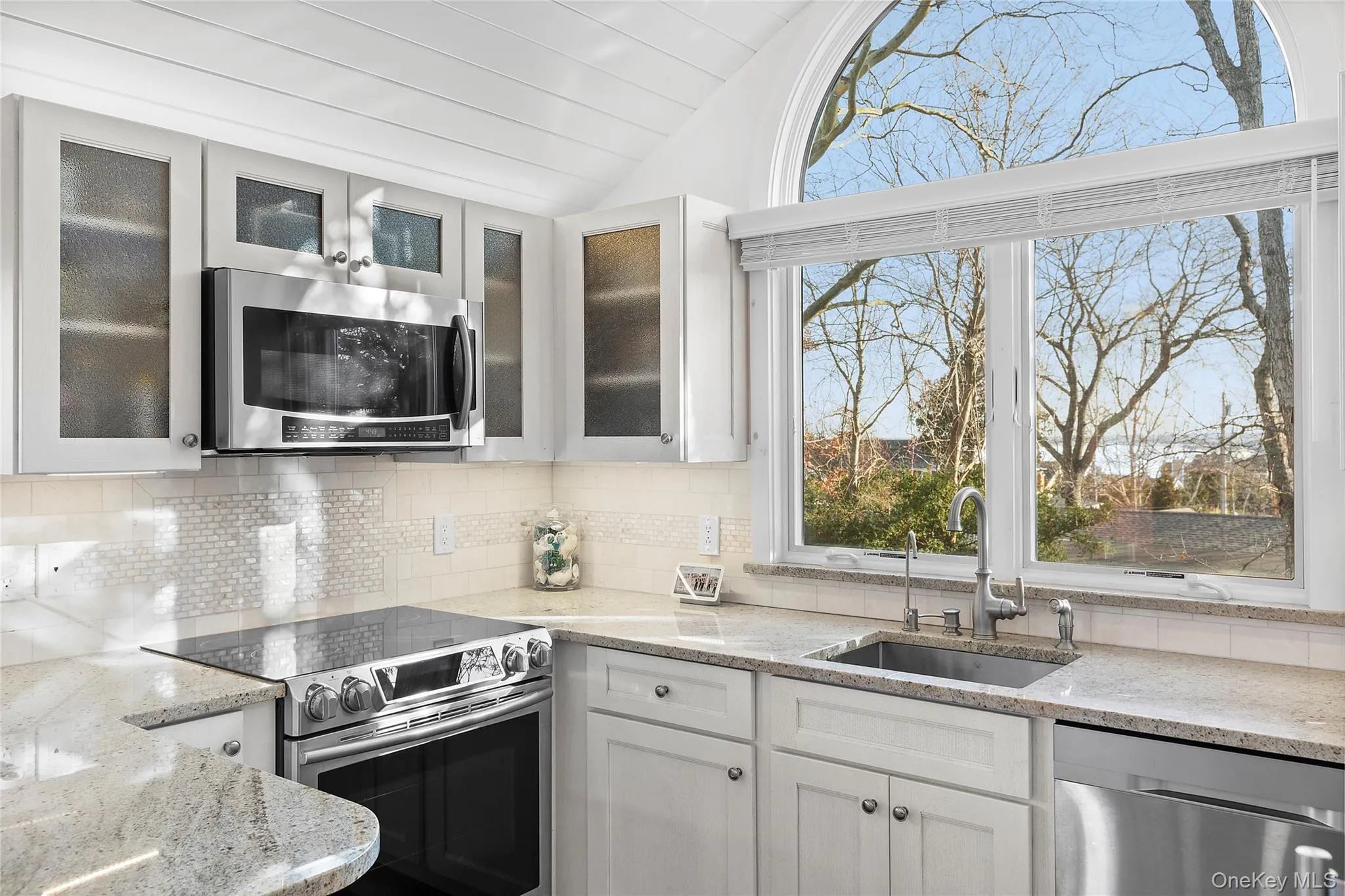 Kitchen with appliances with stainless steel finishes, a sink, lofted ceiling, decorative backsplash, and white cabinets Kitchen with appliances with stainless steel finishes, a sink, lofted ceiling, decorative backsplash, and white cabinets