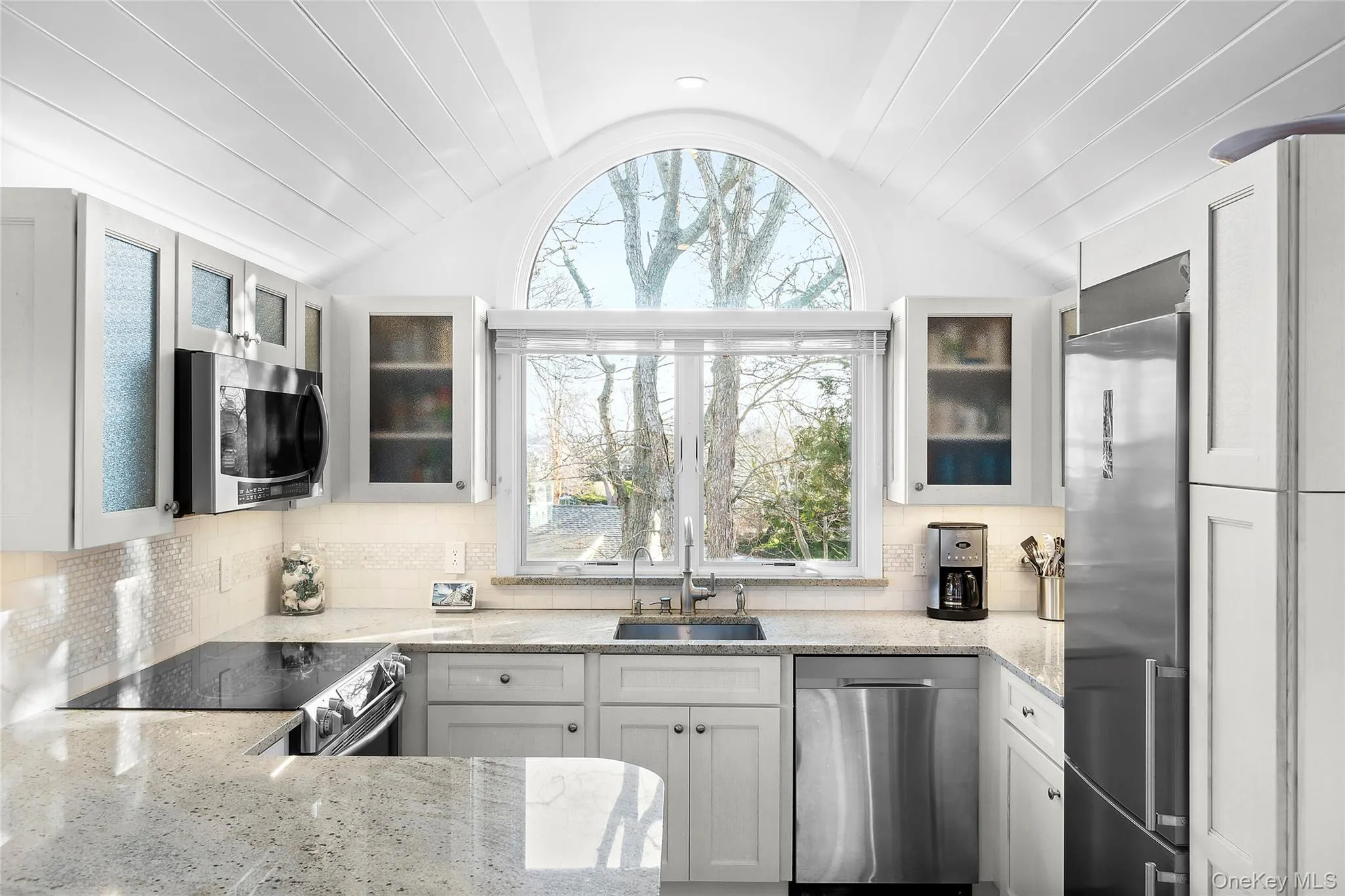 Kitchen featuring a sink, appliances with stainless steel finishes, lofted ceiling, healthy amount of natural light, and light stone counters Kitchen featuring a sink, appliances with stainless steel finishes, lofted ceiling, healthy amount of natural light, and light stone counters