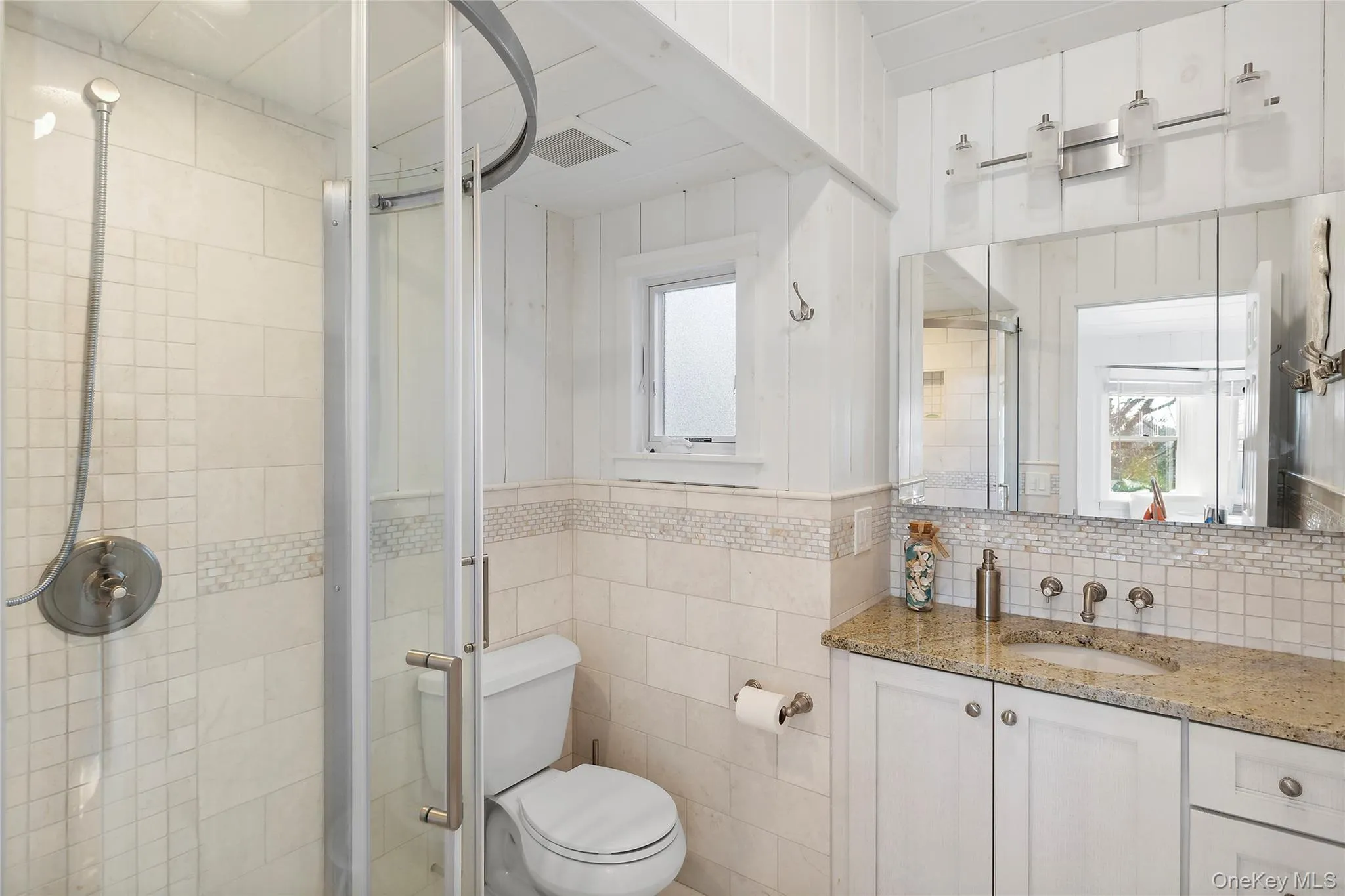 Full bathroom with a shower stall, vanity, tile walls, toilet, and healthy amount of natural light Full bathroom with a shower stall, vanity, tile walls, toilet, and healthy amount of natural light
