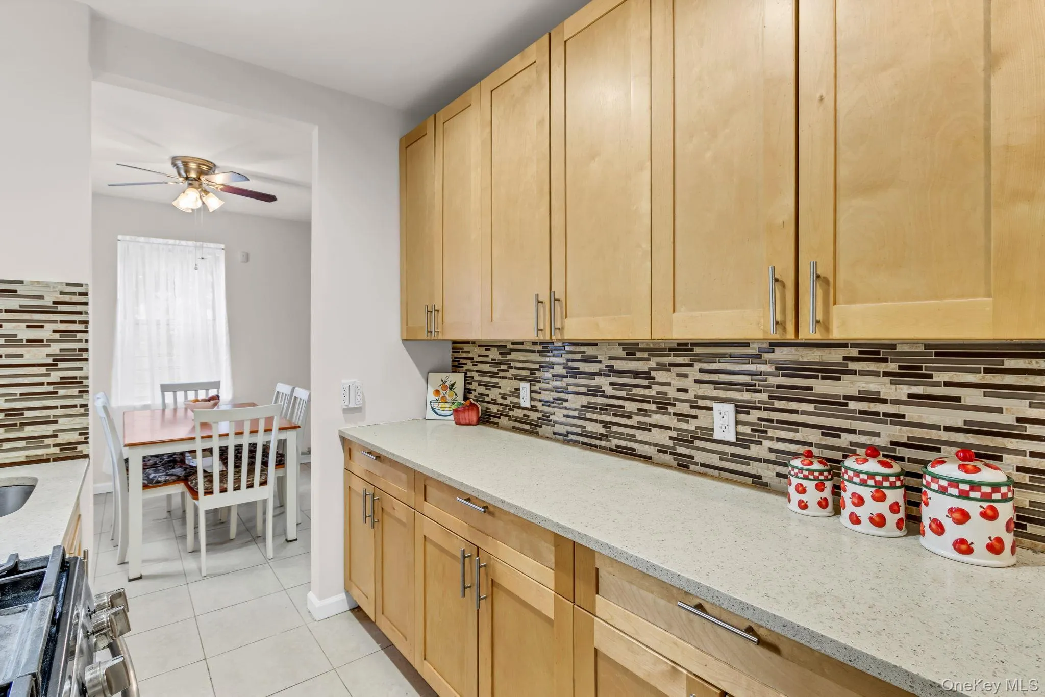 Kitchen featuring light brown cabinetry, a ceiling fan, stainless steel gas range, and decorative backsplash Kitchen featuring light brown cabinetry, a ceiling fan, stainless steel gas range, and decorative backsplash