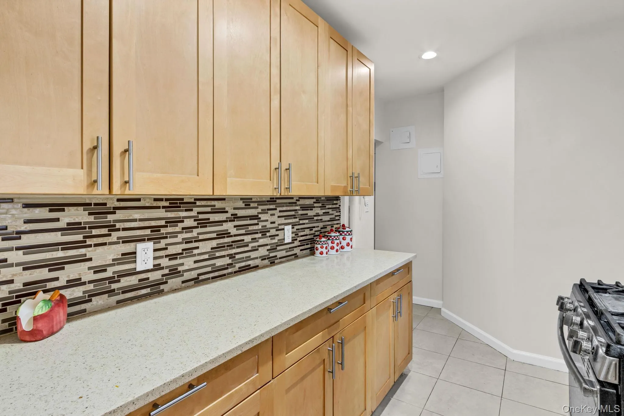 Kitchen with stainless steel gas range oven, decorative backsplash, light tile patterned floors, light stone countertops, and light brown cabinetry Kitchen with stainless steel gas range oven, decorative backsplash, light tile patterned floors, light stone countertops, and light brown cabinetry