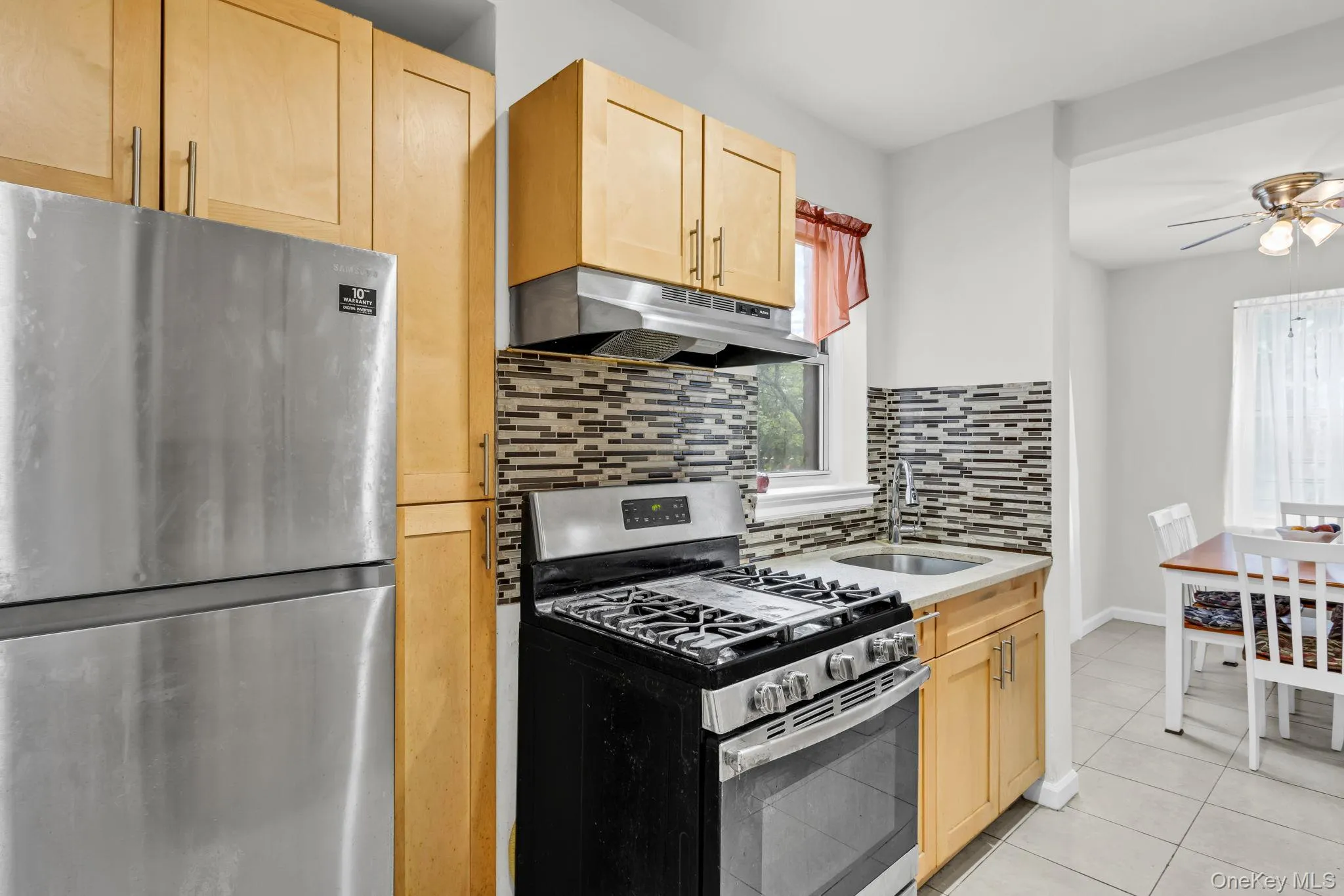 Kitchen featuring stainless steel appliances, under cabinet range hood, light brown cabinetry, a sink, and a ceiling fan Kitchen featuring stainless steel appliances, under cabinet range hood, light brown cabinetry, a sink, and a ceiling fan