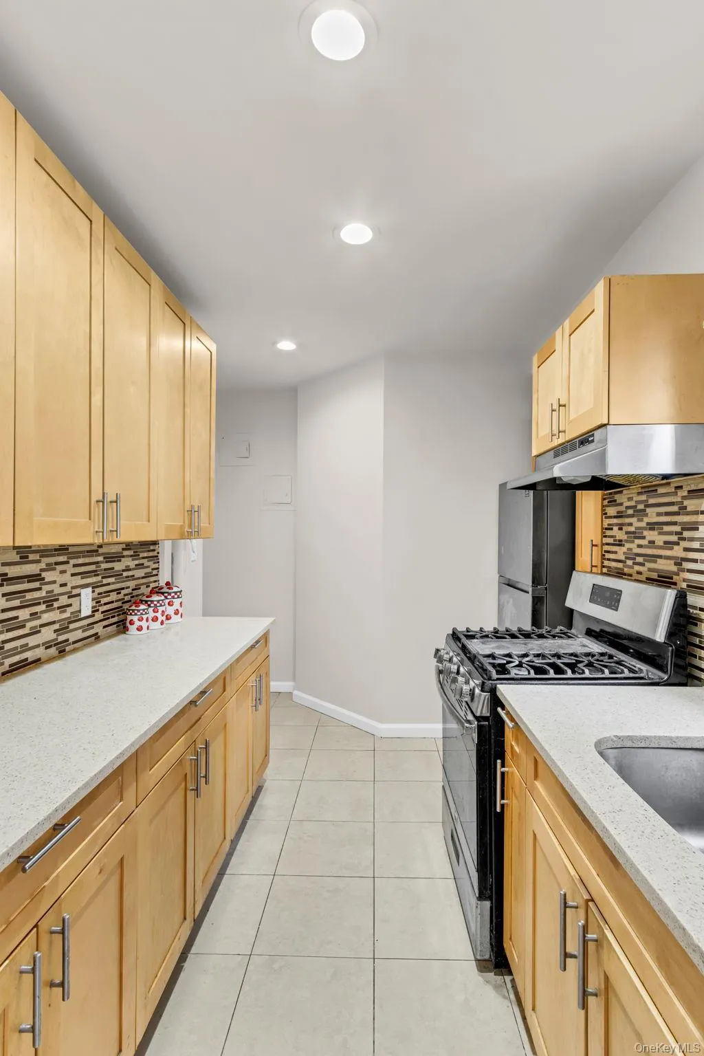 Kitchen with stainless steel gas range oven, under cabinet range hood, light brown cabinetry, baseboards, and decorative backsplash Kitchen with stainless steel gas range oven, under cabinet range hood, light brown cabinetry, baseboards, and decorative backsplash