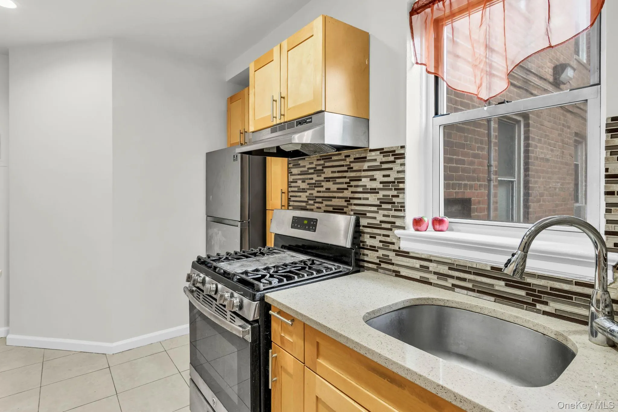 Kitchen with under cabinet range hood, stainless steel appliances, a sink, light tile patterned floors, and tasteful backsplash Kitchen with under cabinet range hood, stainless steel appliances, a sink, light tile patterned floors, and tasteful backsplash