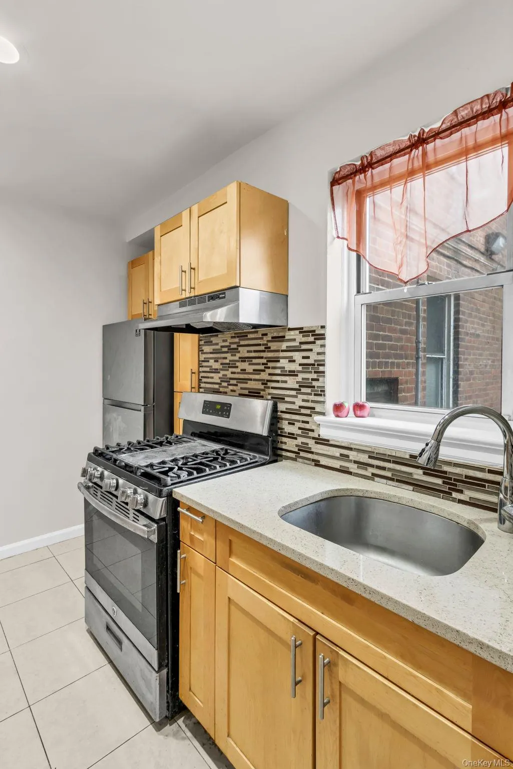 Kitchen with appliances with stainless steel finishes, under cabinet range hood, a sink, light brown cabinets, and tasteful backsplash Kitchen with appliances with stainless steel finishes, under cabinet range hood, a sink, light brown cabinets, and tasteful backsplash