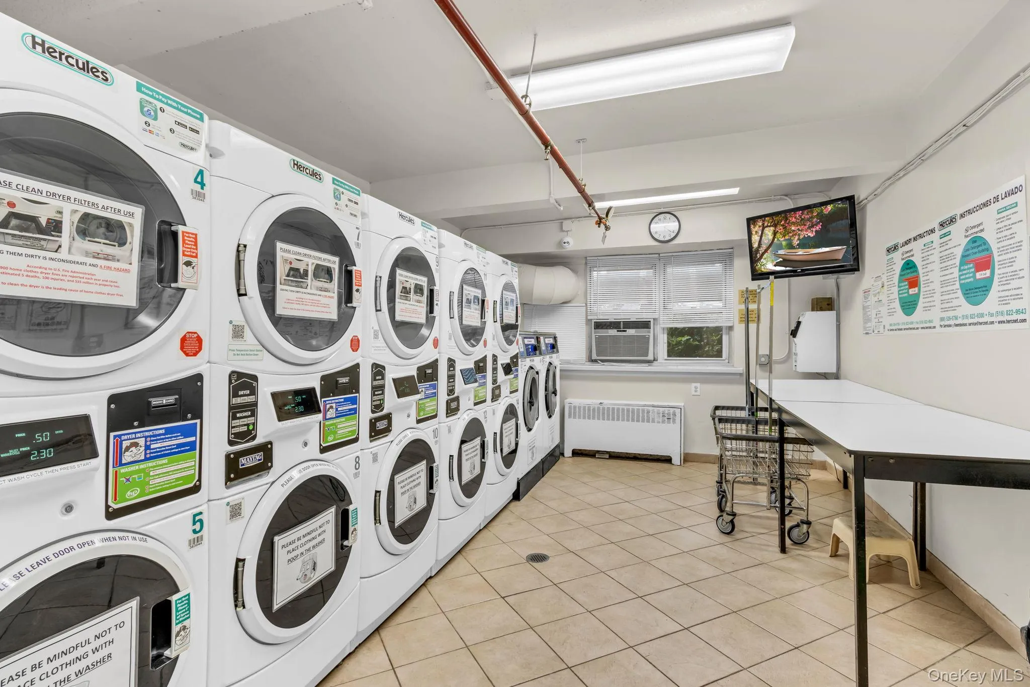 Shared laundry featuring stacked washing machine and dryer, radiator, washer and clothes dryer, and light tile patterned floors Shared laundry featuring stacked washing machine and dryer, radiator, washer and clothes dryer, and light tile patterned floors