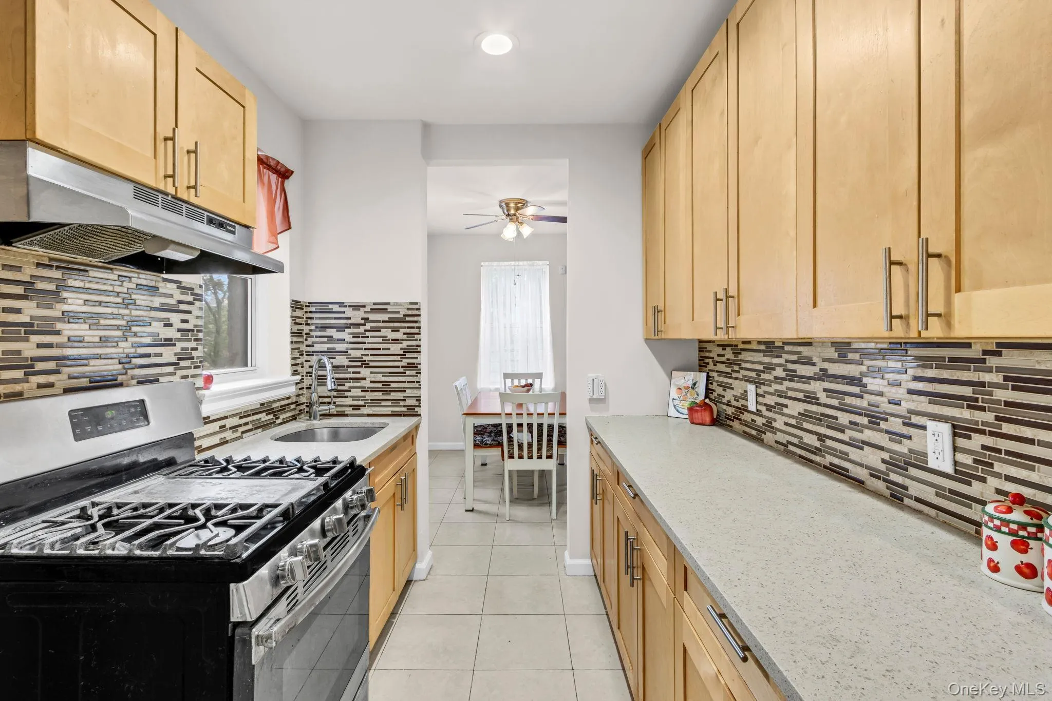 Kitchen with stainless steel range with gas stovetop, under cabinet range hood, tasteful backsplash, a sink, and light tile patterned floors Kitchen with stainless steel range with gas stovetop, under cabinet range hood, tasteful backsplash, a sink, and light tile patterned floors