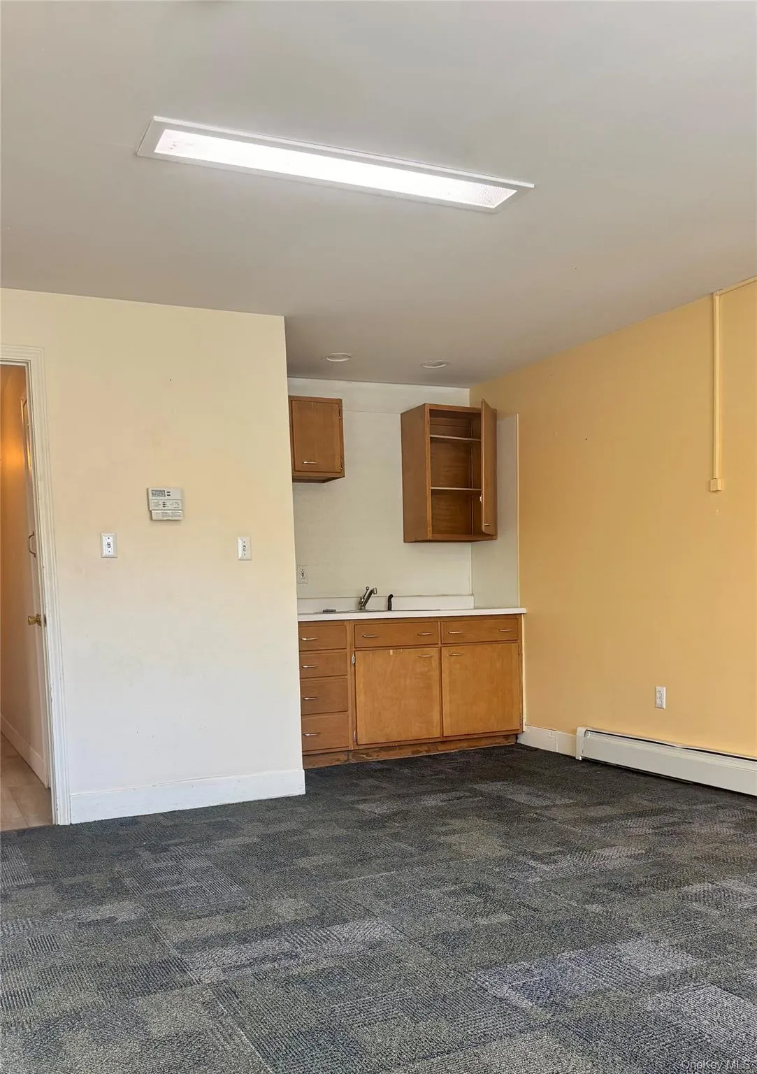 Kitchen with light countertops, brown cabinets, a baseboard radiator, dark carpet, and open shelves Kitchen with light countertops, brown cabinets, a baseboard radiator, dark carpet, and open shelves