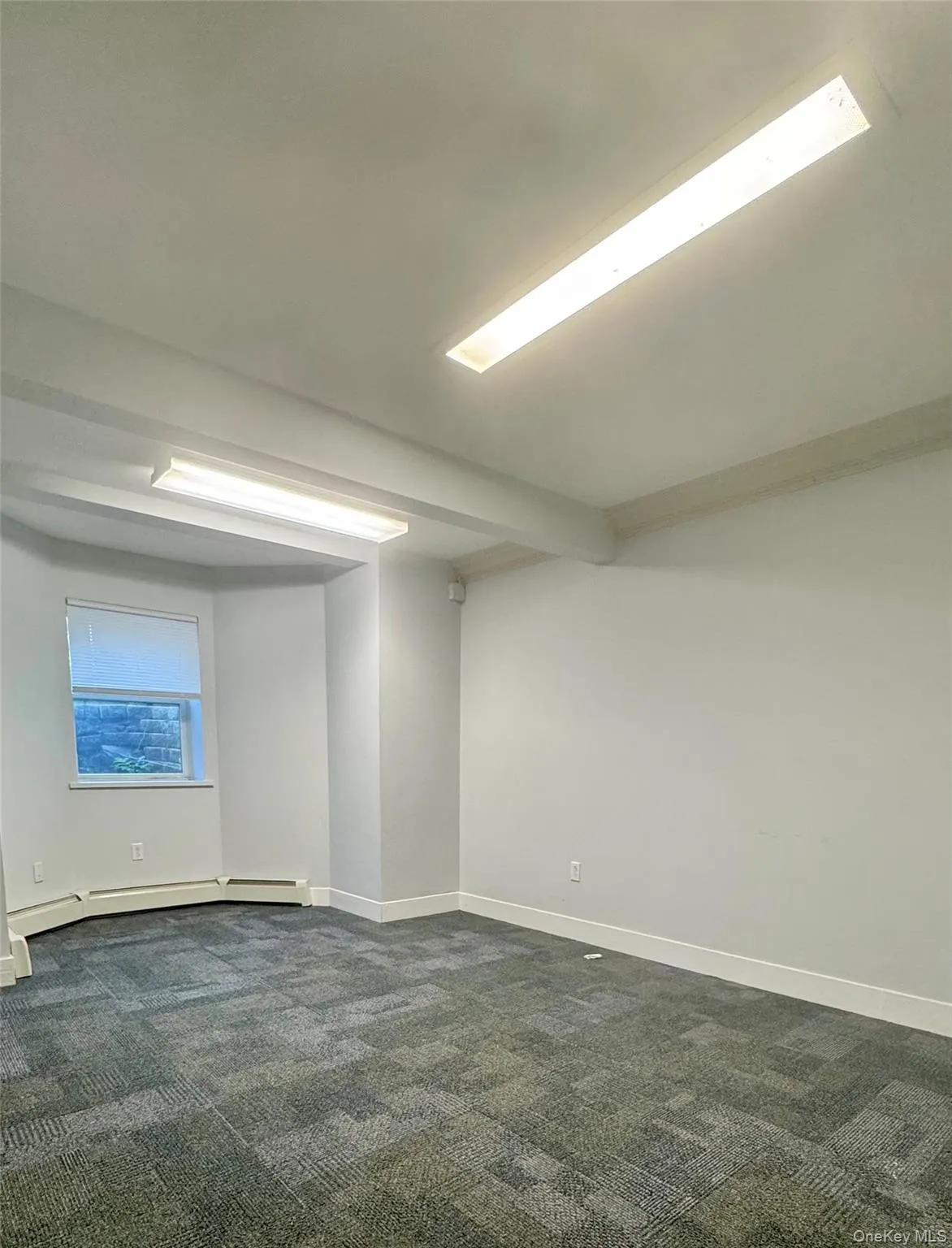 Unfurnished room with dark colored carpet, a baseboard heating unit, and beamed ceiling Unfurnished room with dark colored carpet, a baseboard heating unit, and beamed ceiling