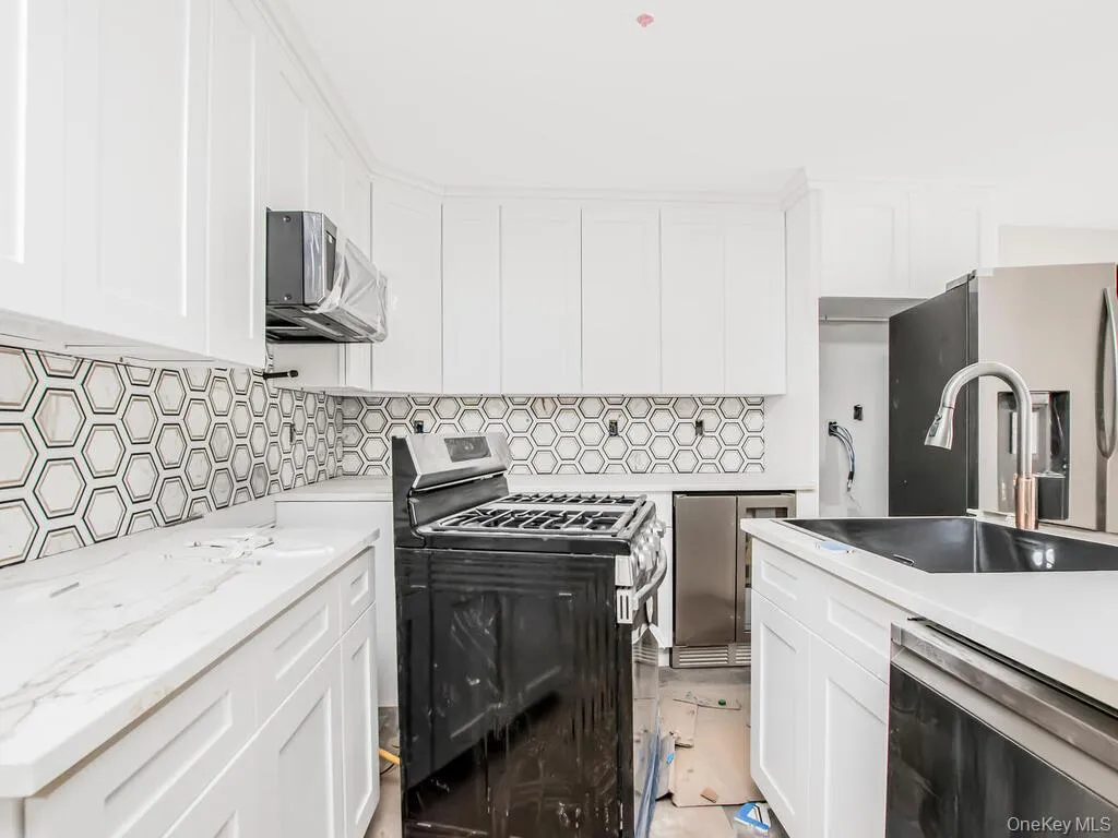 Kitchen featuring stainless steel appliances, a sink, backsplash, and white cabinetry Kitchen featuring stainless steel appliances, a sink, backsplash, and white cabinetry