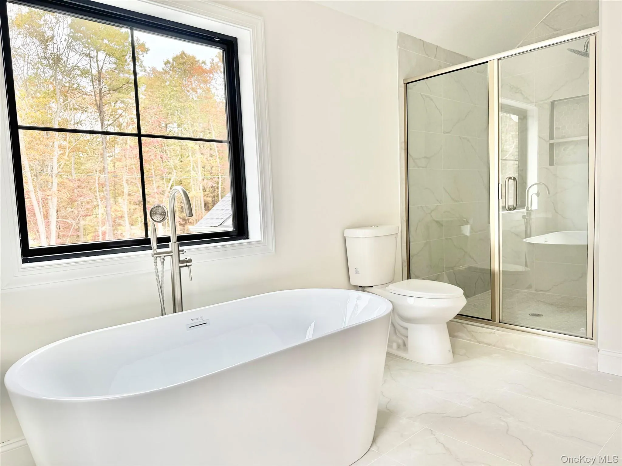 Bathroom with a freestanding tub, marble finish flooring, and plenty of natural light Bathroom with a freestanding tub, marble finish flooring, and plenty of natural light